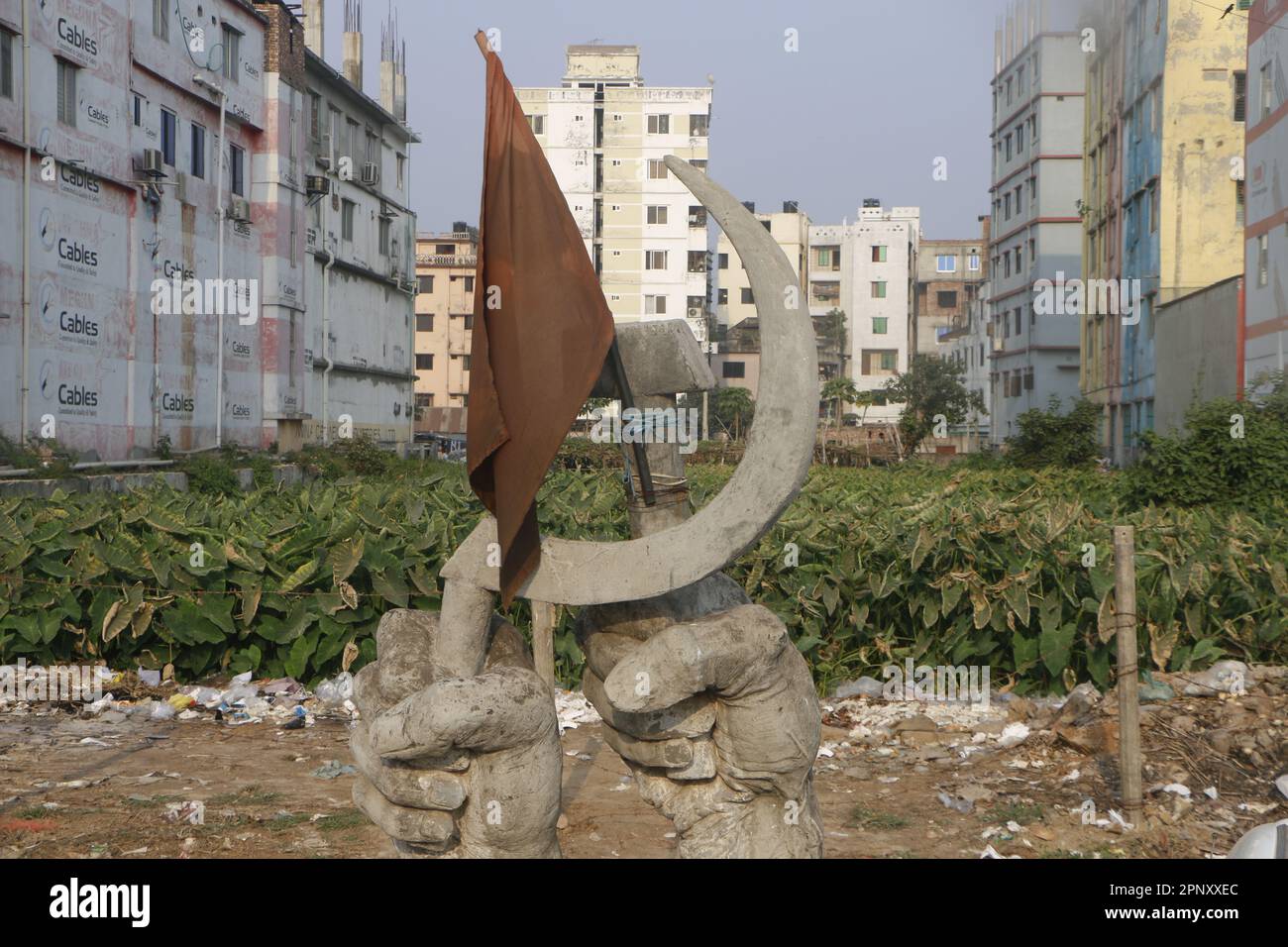 Sabhar, Bangladesh. 20th Apr, 2023. Il monumento 'Protibade-Protirodh' (protesta-resistenza) è stato eretto da un gruppo di giovani nell'agosto 2013 per commemorare le vittime del crollo di Rana Plaza. La bandiera rossa posta sul semplice monumento con due mani muscolari - una con una falce, l'altra con un martello - si stava sbiadendo. Sullo sfondo, le piante di arum selvatico crescono nel luogo in cui l'edificio a otto piani è crollato il 24 aprile 2014. (A dpa: Dieci anni fa, Rana Plaza divenne un simbolo della sofferenza dei lavoratori) Credit: Nazrul Islam/dpa/Alamy Live News Foto Stock