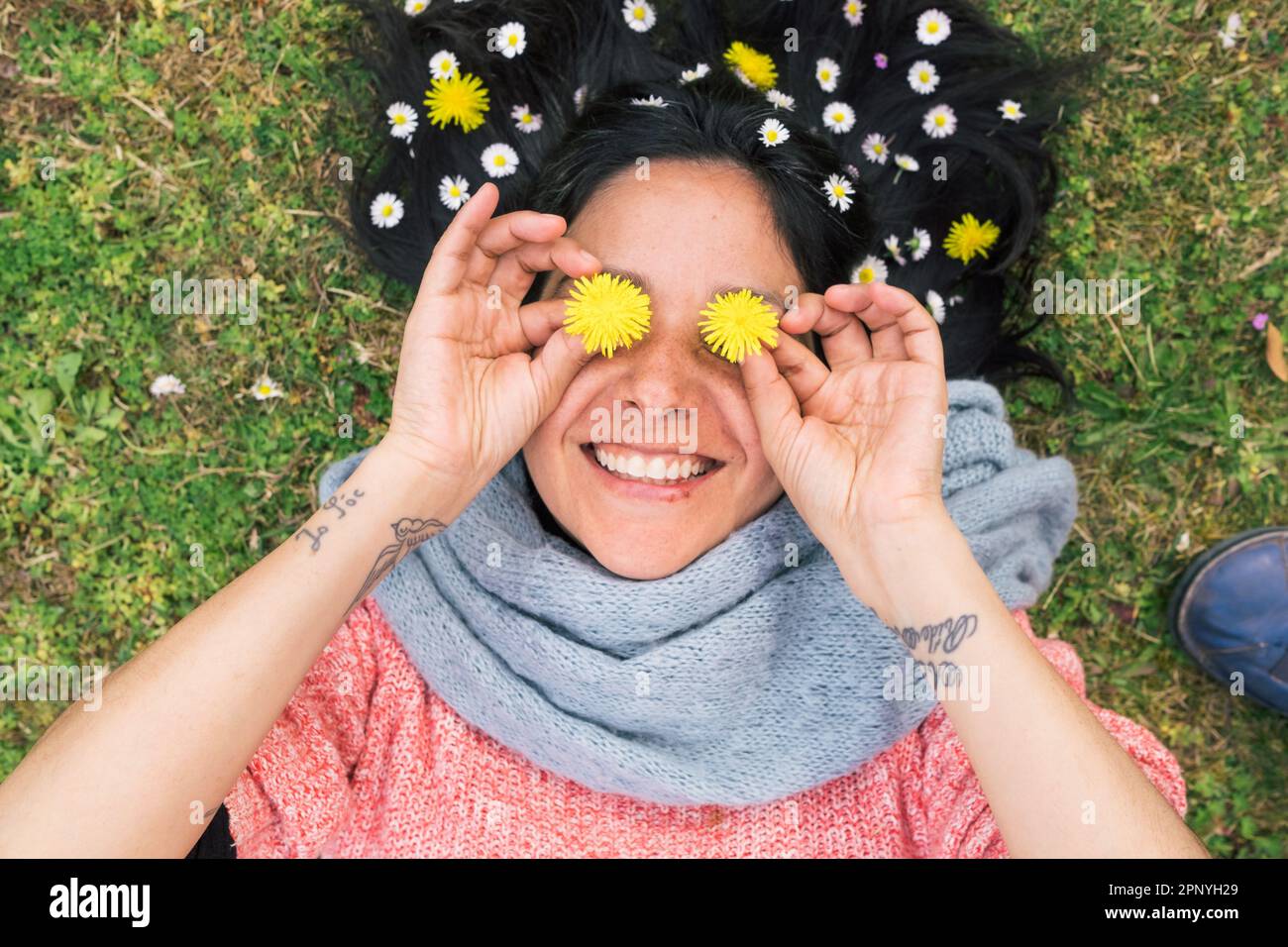 Donna sorridente sdraiata sull'erba con fiori nei suoi capelli e occhi, rilassato e divertente.concetto di primavera relax e connessione con la natura. Vista dall'alto. Foto Stock