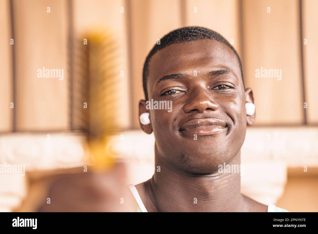 Primo piano ritratto di un giovane e attraente uomo nero sorridente alla fotocamera indossando cuffie wireless e tenendo un pennello nel forgroun Foto Stock