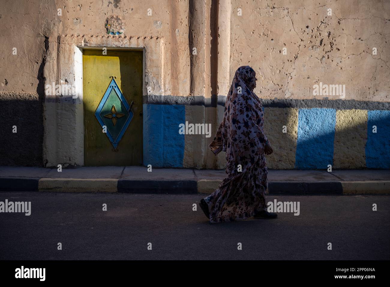 Silhouette di una donna che cammina di fronte alla porta di una casa decorata con colorati motivi tradizionali berberi. Foto Stock