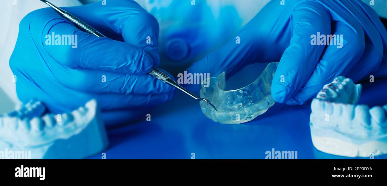 un dentista sta regolando una stecca occlusale, usando uno strumento di metallo, in un formato panoramico da usare come banner web o intestazione Foto Stock