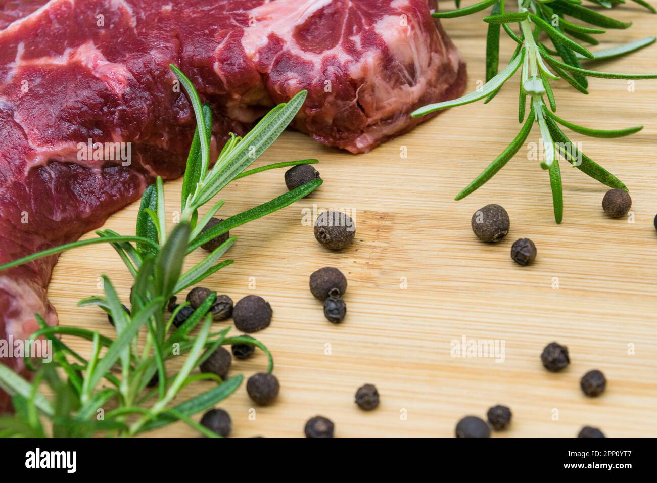 Bistecca di manzo, vista di manzo fresco su un asse di legno con rosmarino, pepe nero, foglia di gabinetto. Foto Stock