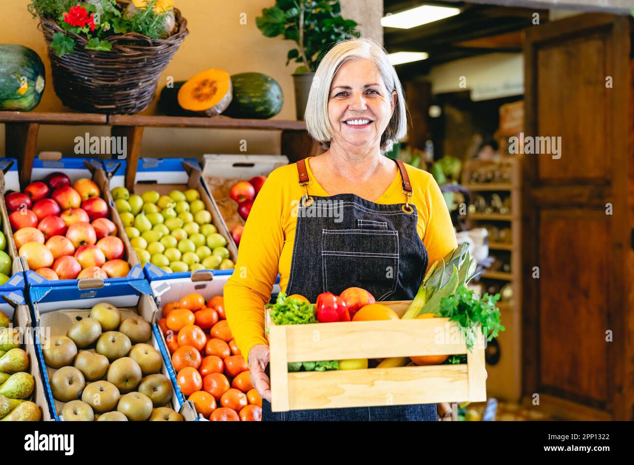 Fruttivendolo femminile che lavora sul mercato con una scatola contenente frutta e verdura fresca - concetto di vendita al dettaglio di alimenti Foto Stock
