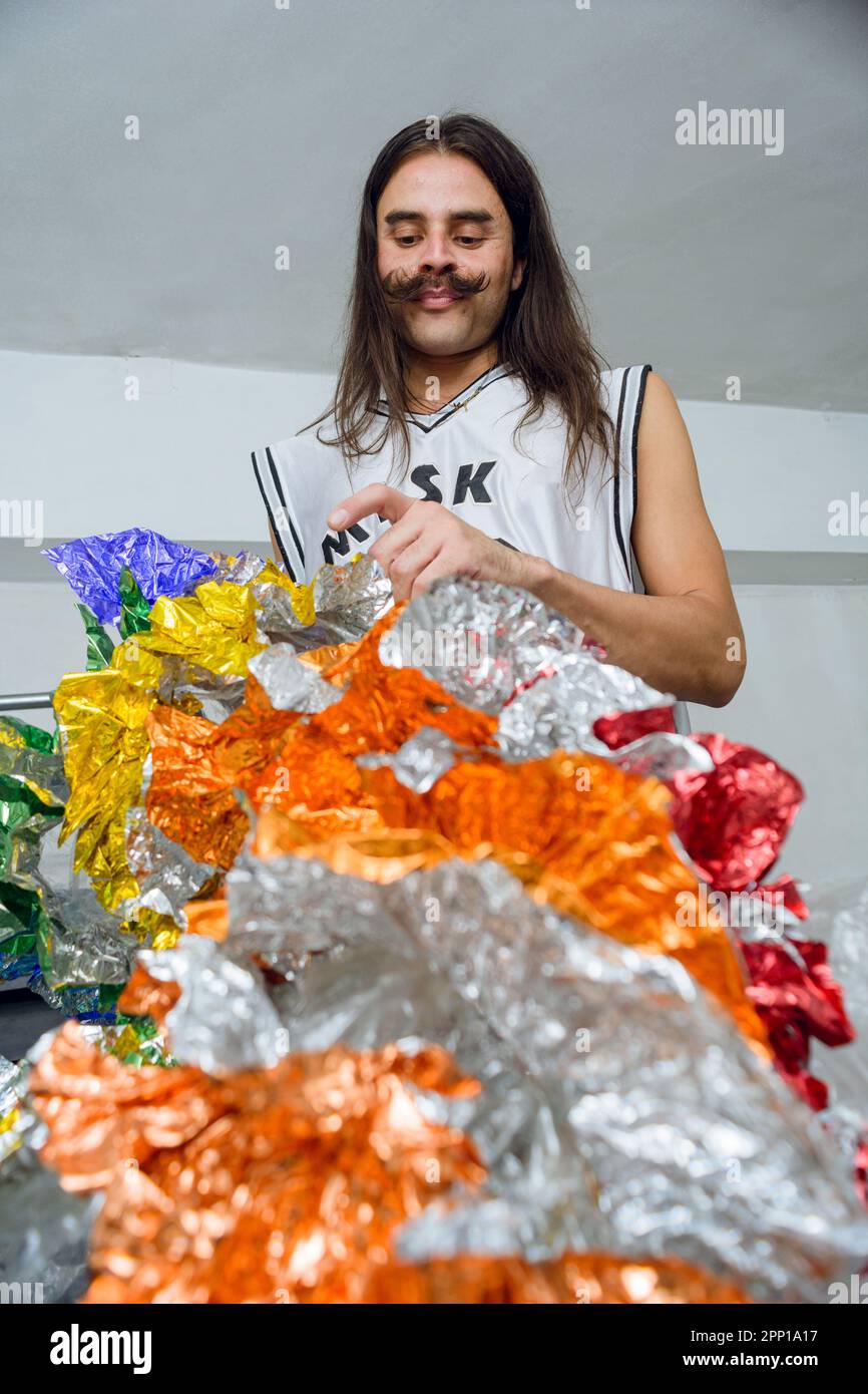 ritratto di latino non-binario nella sua stanza finendo facendo il suo costume colorato drag queen fatto di materiale riciclato Foto Stock