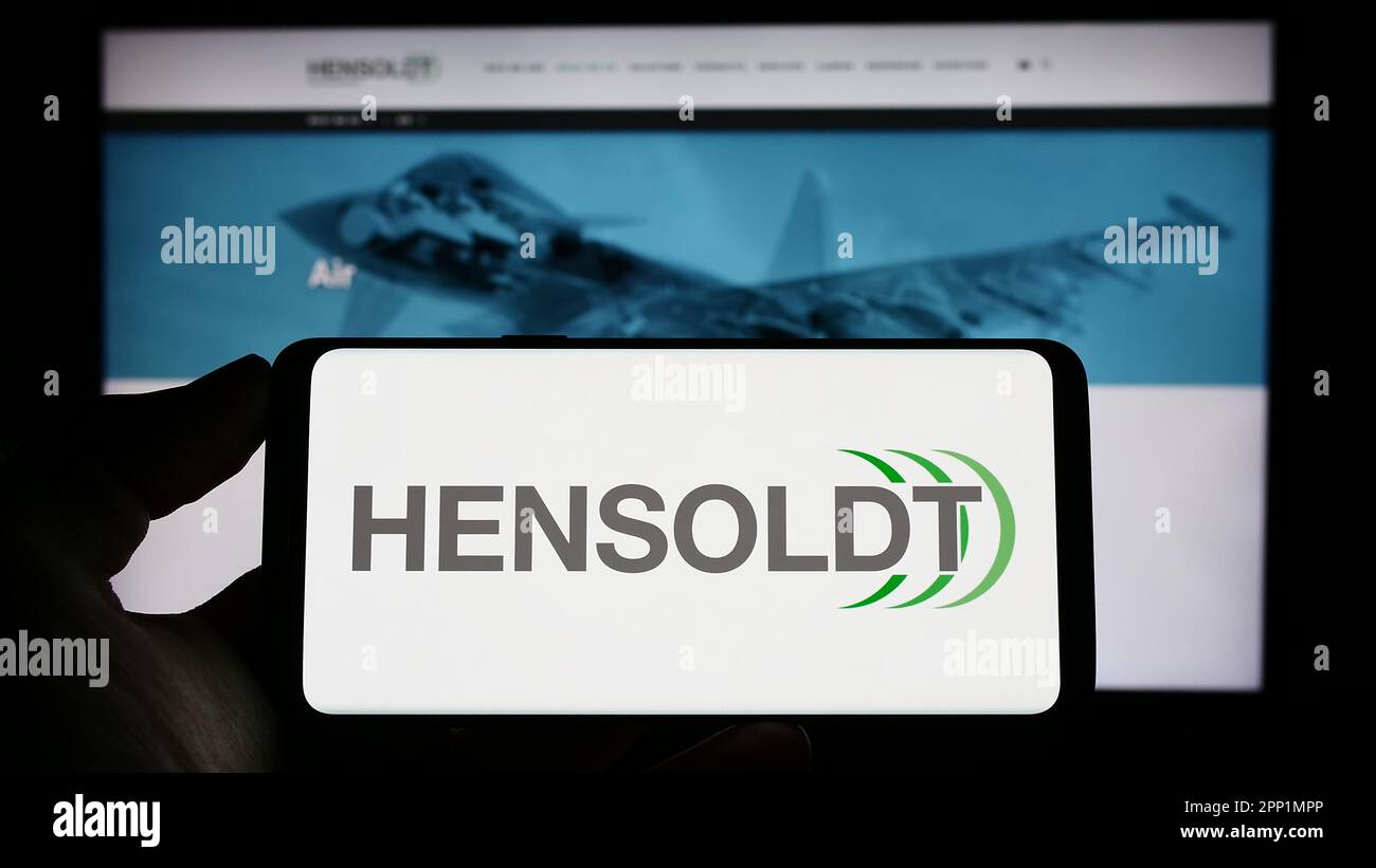 Persona che tiene il cellulare con il logo della società tedesca di difesa Hensoldt AG sullo schermo di fronte al sito web aziendale. Messa a fuoco sul display del telefono. Foto Stock