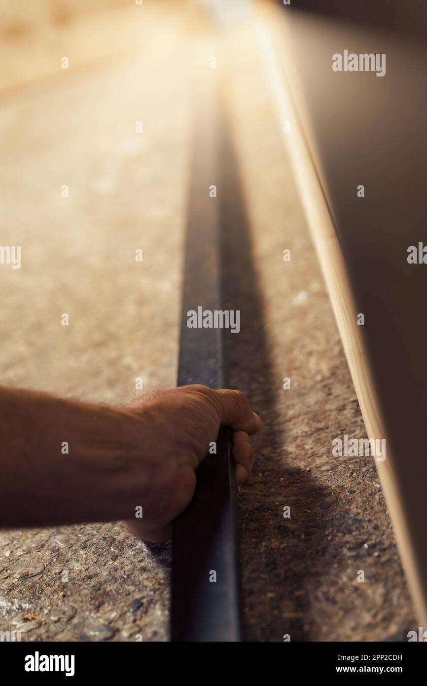 La mano forte di un falegname afferra saldamente un utensile metallico per facilitare un lavoro pesante nella costruzione di mobili. La luce solare calda fluisce in t Foto Stock