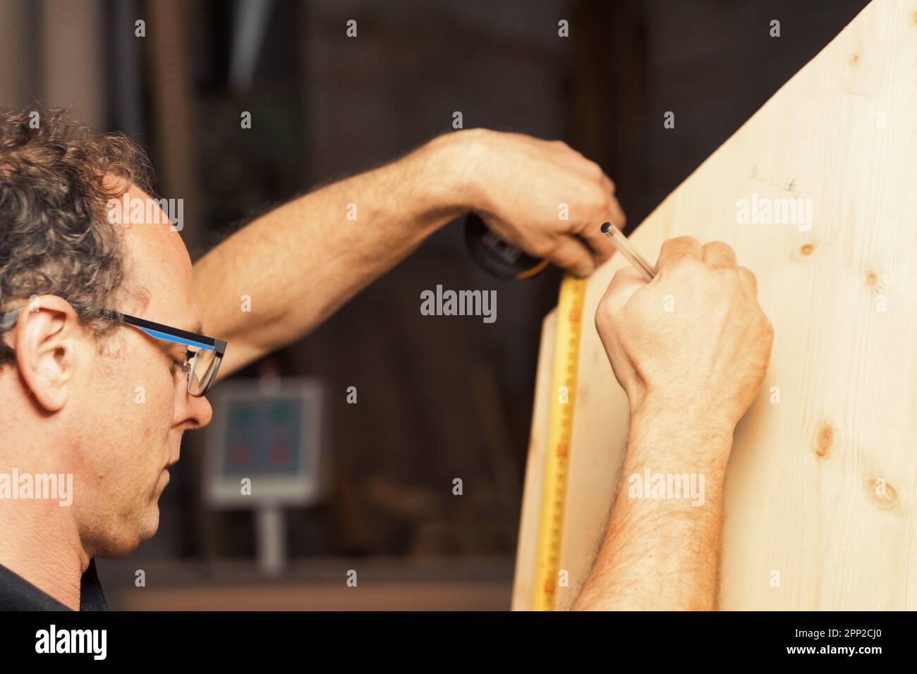 Un artigiano del legno traccia le linee e le misure nel suo negozio di legno luminoso. Egli è concentrato e competente, la sua esperienza è tutto personale e. Foto Stock