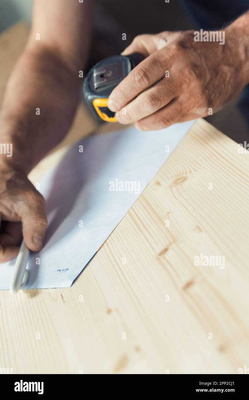 Il falegname tiene un metro a nastro in una mano e appoggia una penna su un asse di legno ruvido con l'altra. Design e preparazione fanno parte del suo lavoro: Foto Stock