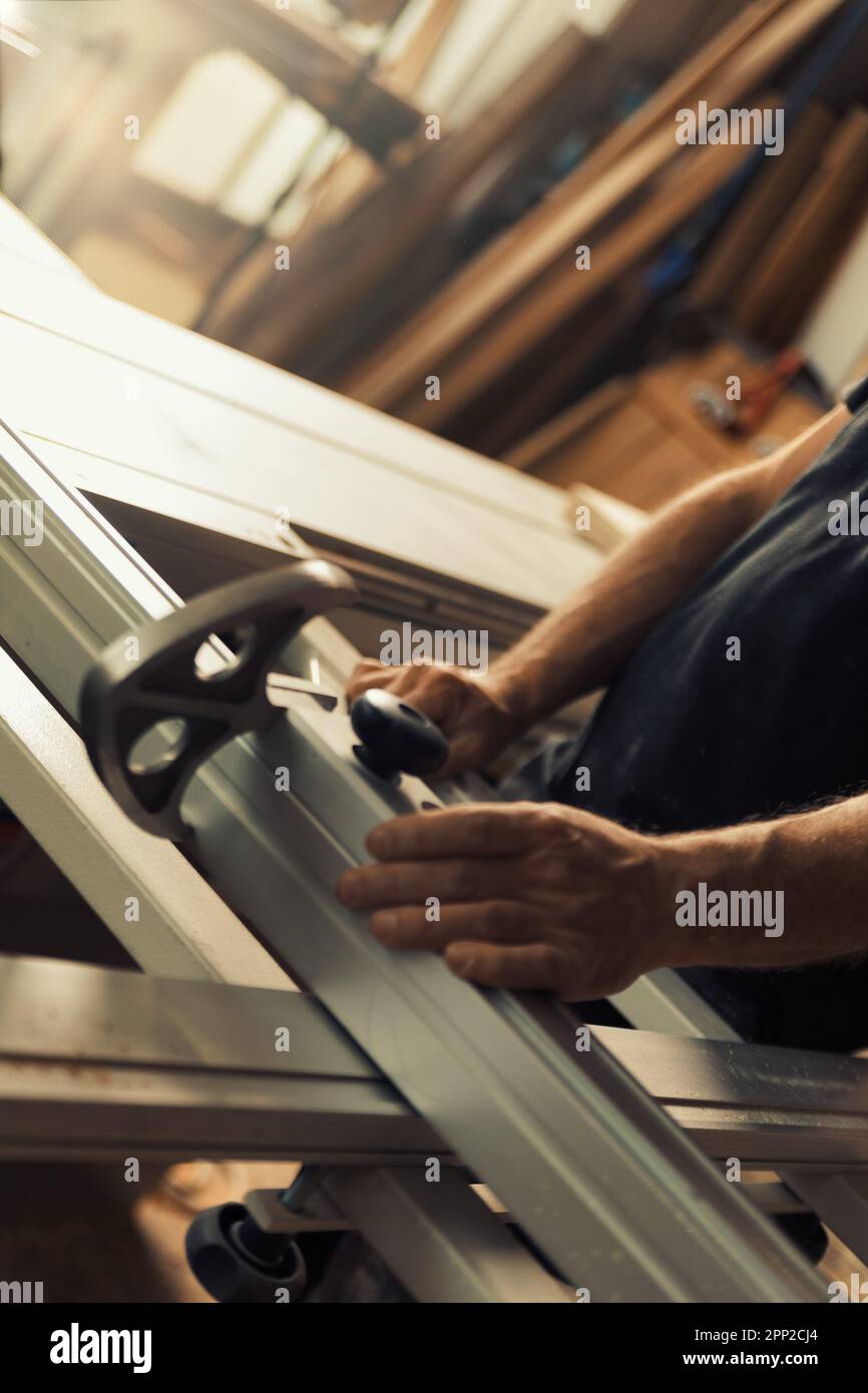 n un'officina di lavorazione del legno, un uomo sta posizionando una mensola o un asse di legno su una macchina di lavorazione del legname. Mani maschio forti e grandi quantità di legno sono v Foto Stock