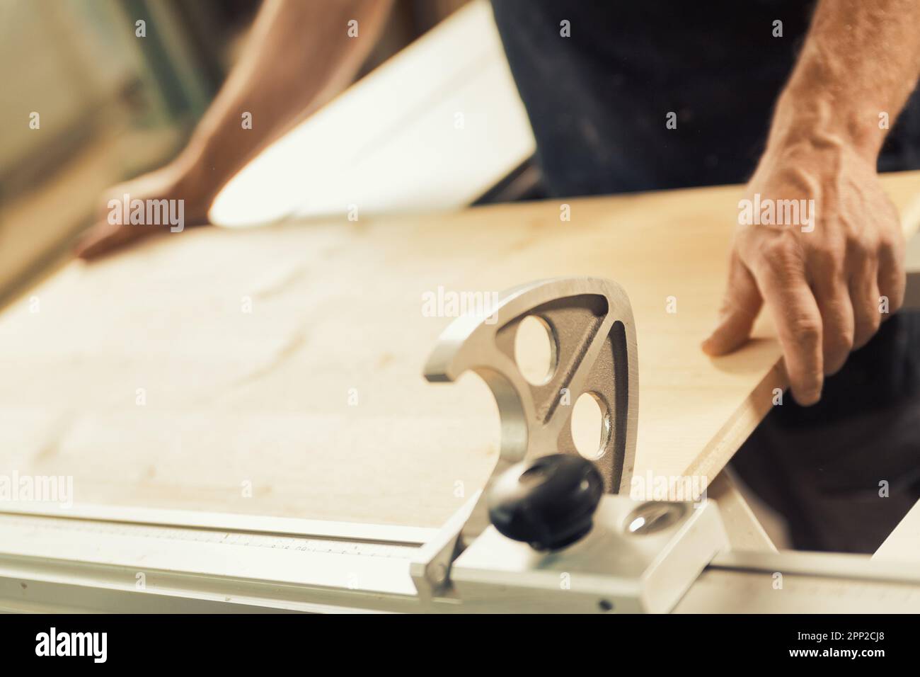 n un'officina di lavorazione del legno, un uomo sta posizionando una mensola o un asse di legno su una macchina di lavorazione del legname. Mani maschio forti e grandi quantità di legno sono v Foto Stock