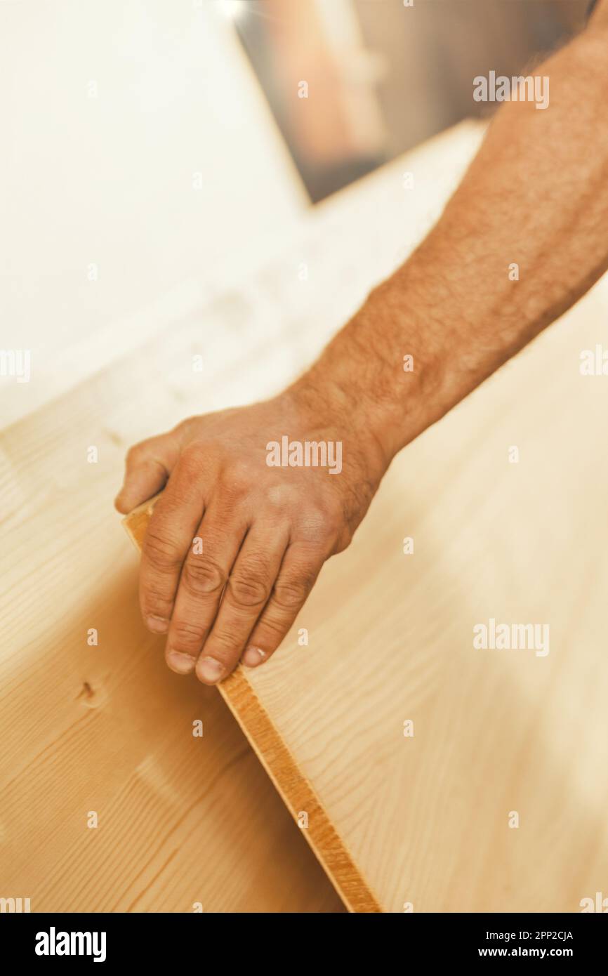La mano forte di un uomo solleva con forza e precisione un grande asse di legno. La messa a fuoco è sulla mano, mentre il resto è in sfocatura selettiva Foto Stock