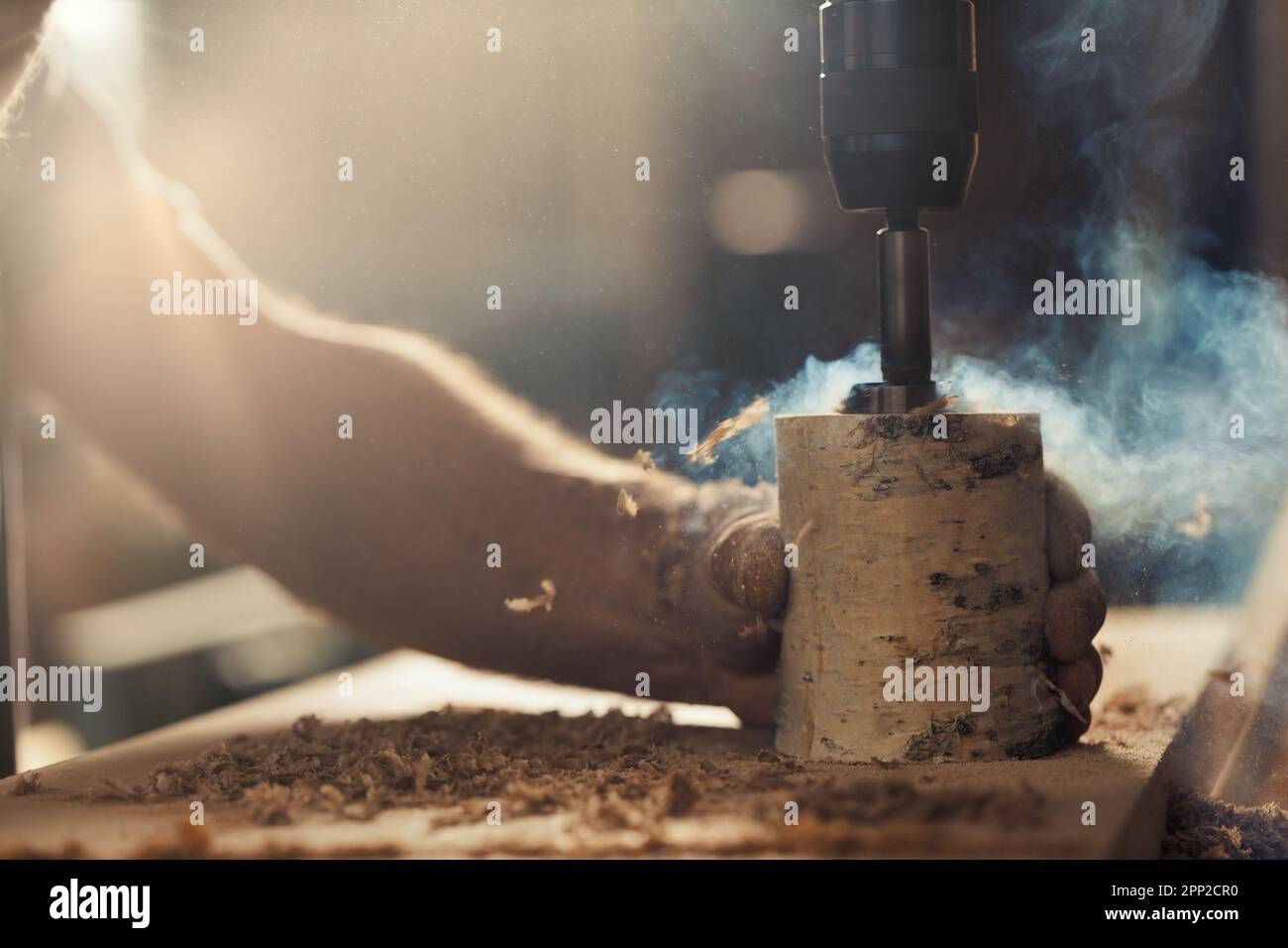 La mano forte del falegname tiene saldamente un tronco di betulla mentre si usa una pressa per trapano per intagliarlo, abbassando la leva con l'altro braccio. Le opere artigianali Foto Stock