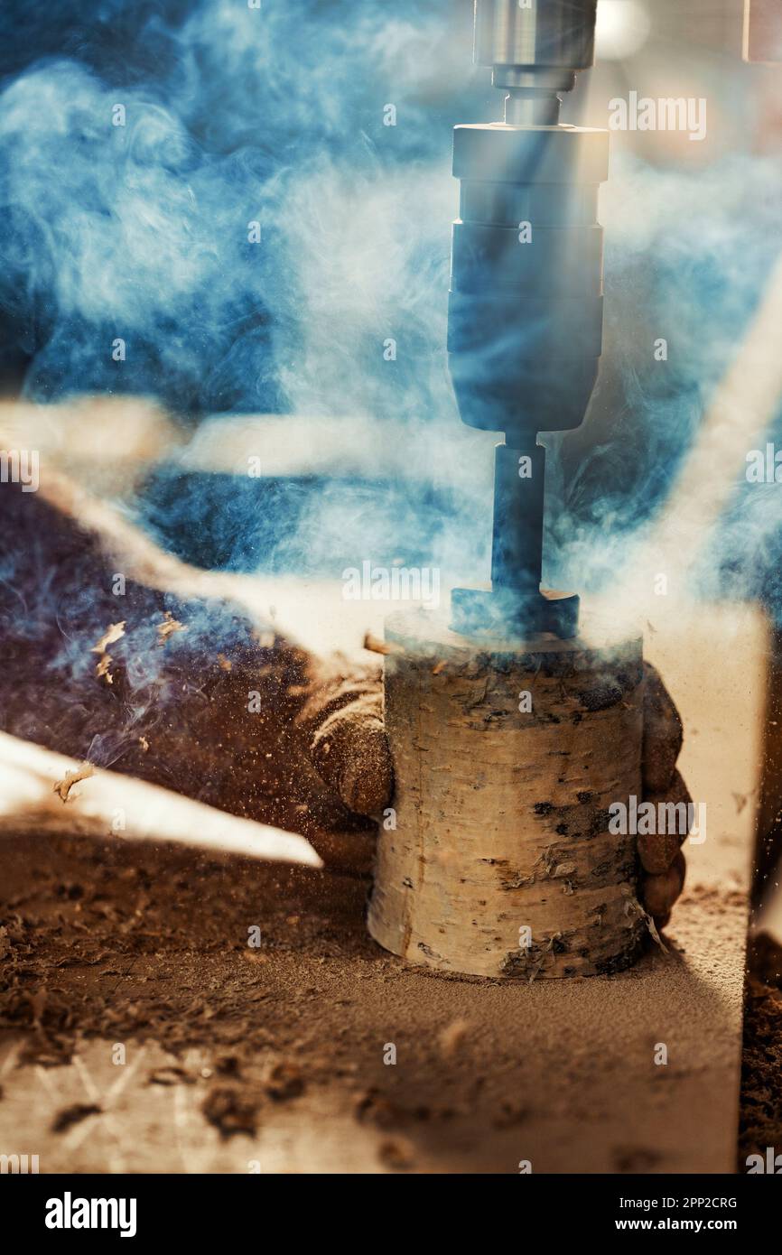 La mano forte del falegname tiene saldamente un tronco di betulla mentre si usa una pressa per trapano per intagliarlo, abbassando la leva con l'altro braccio. Le opere artigianali Foto Stock