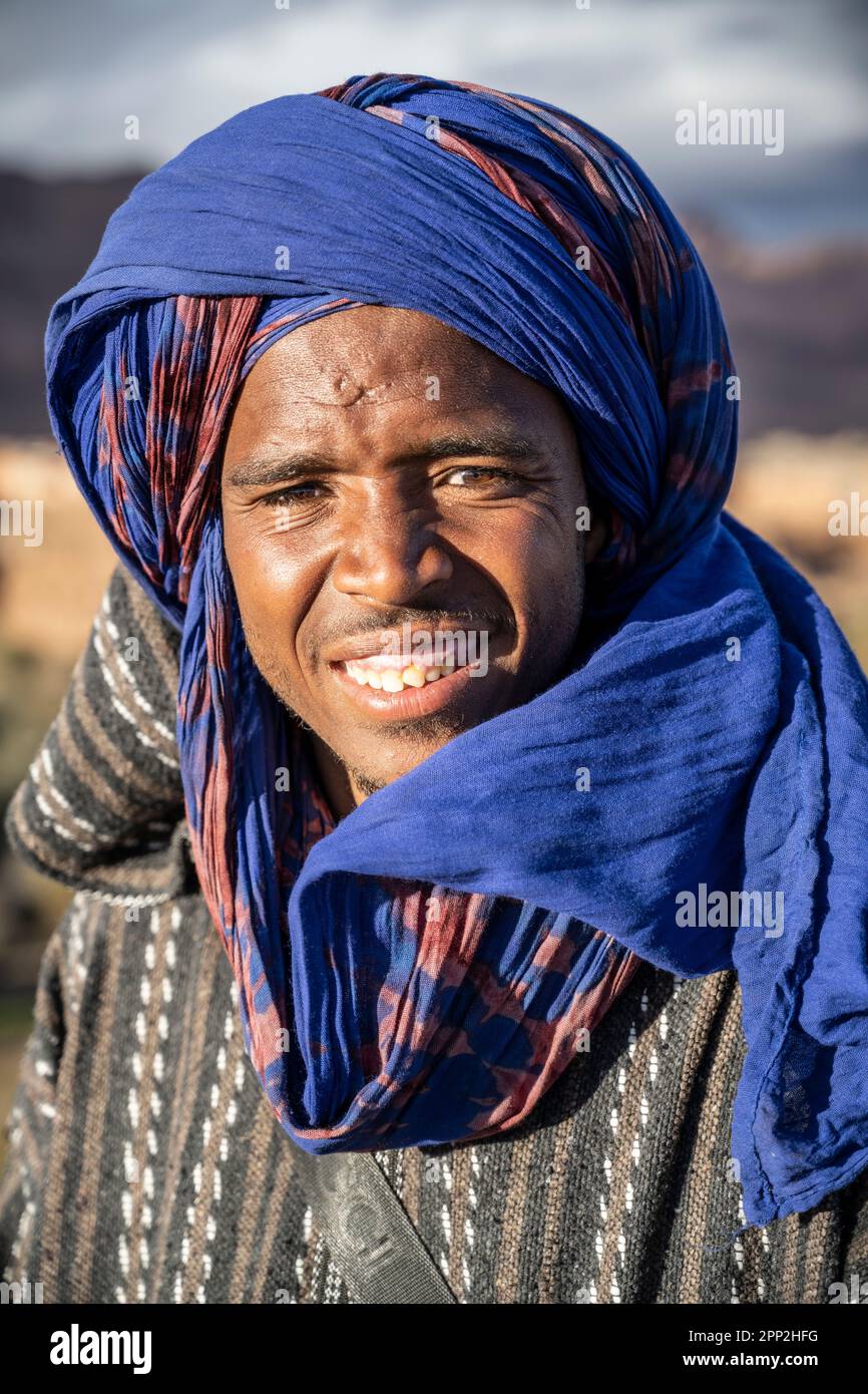 Ritratto di un giovane vestito con gli abiti tipici dei nomadi berberi accanto ad un punto di vista sull'oasi di Tinghir. Foto Stock