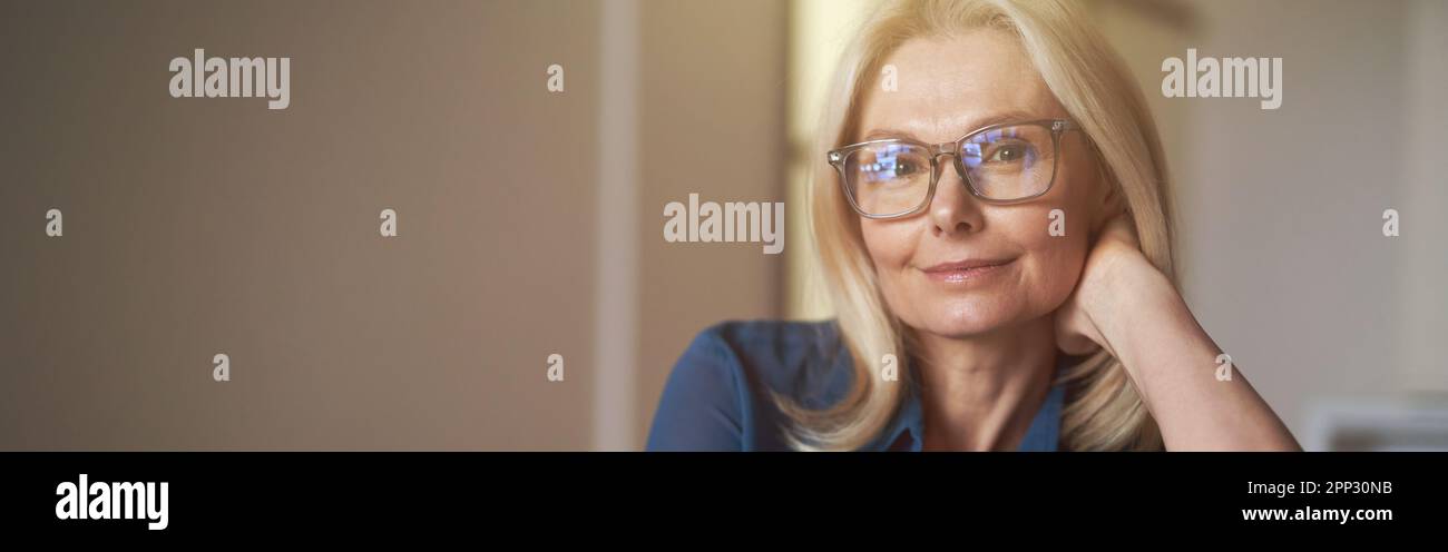 Ritratto interno di attraente donna matura con piacevole sorriso rilassante sul divano nel suo appartamento moderno Foto Stock