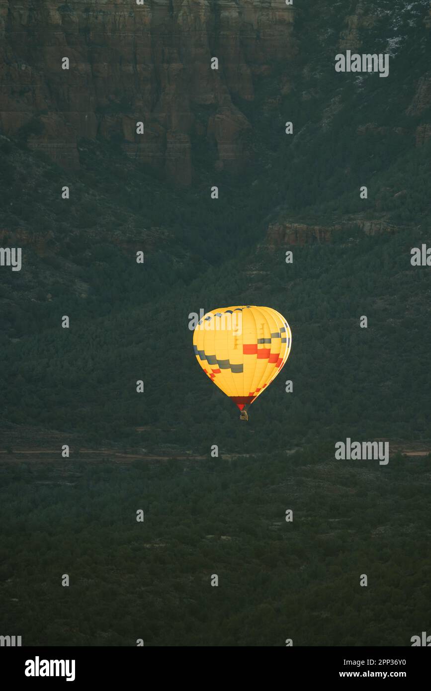 Immagine verticale del teleobiettivo di palloncino giallo ad aria calda che rilascia fiamme isolate contro lo sfondo scuro del pavimento della valle durante il volo mattutino. Foto Stock