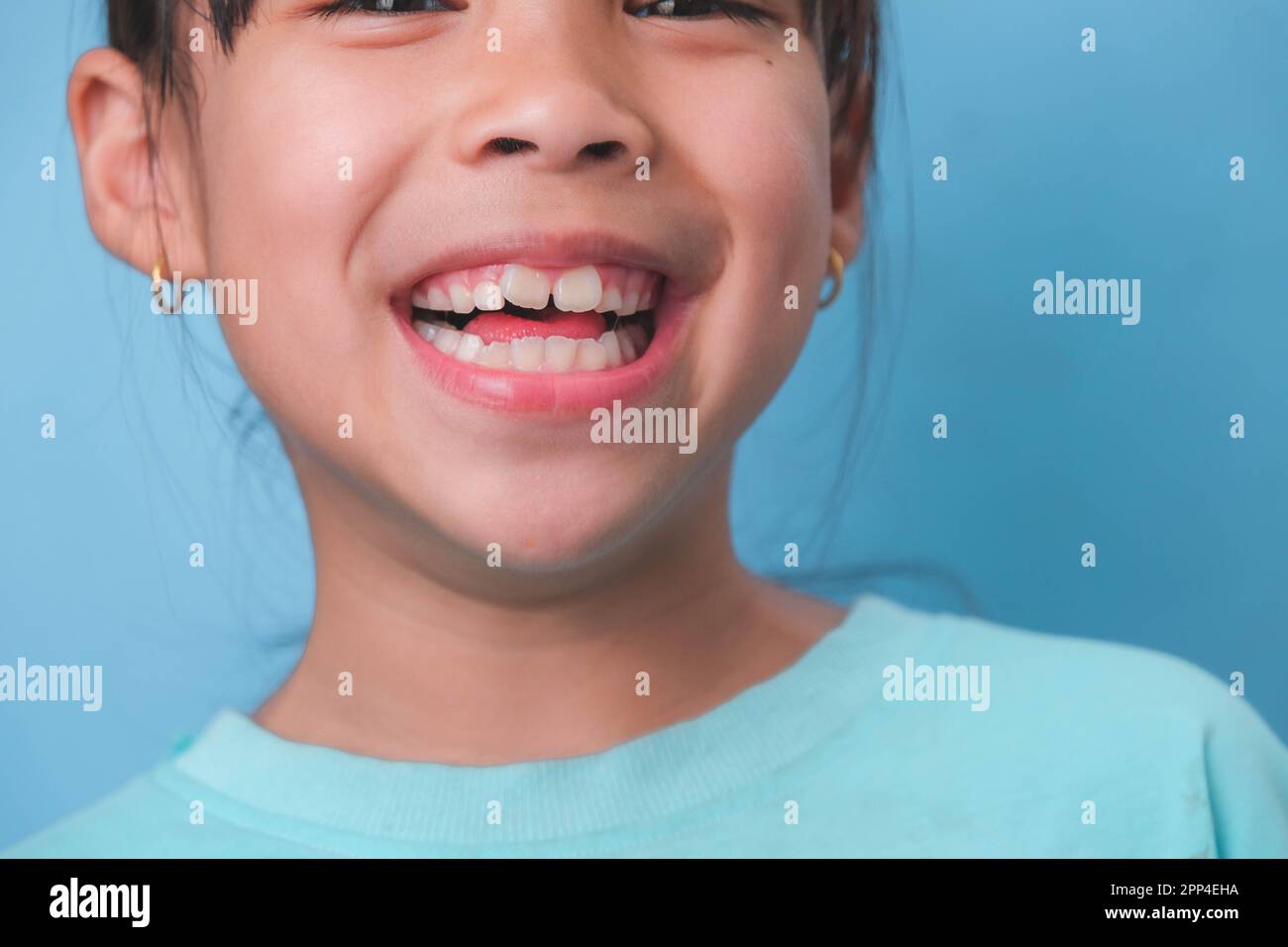 Primo piano di una giovane ragazza sorridente che rivela i suoi bei denti bianchi su uno sfondo blu. Concetto di buona salute nell'infanzia. Foto Stock