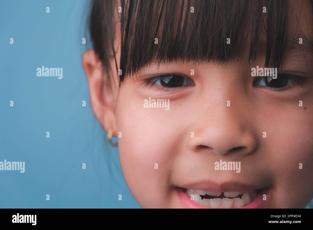 Ritratto di una bambina sorridente che guarda la fotocamera. Primo piano di cute ragazza asiatica faccia posa su sfondo blu. Foto Stock