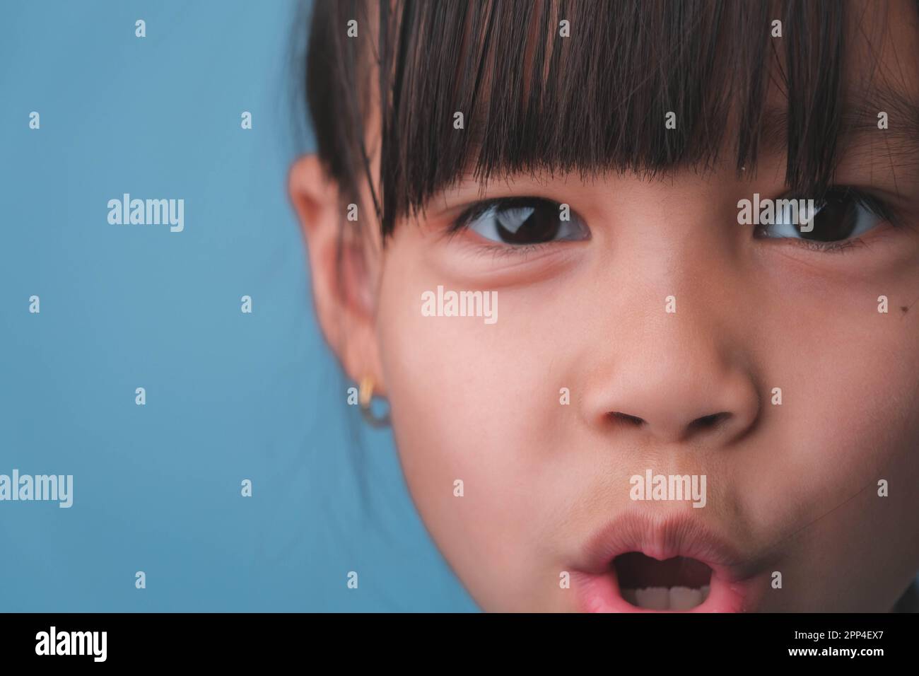 Ritratto di una bambina sorridente che guarda la fotocamera. Primo piano di cute ragazza asiatica faccia posa su sfondo blu. Foto Stock