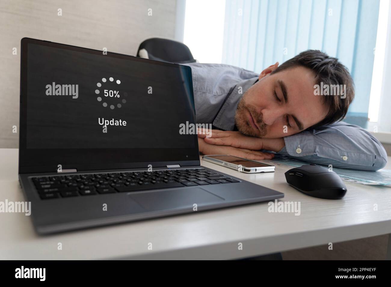 Un nuovo aggiornamento del sistema operativo. il software è in fase di aggiornamento. Il dipendente è stanco e dorme sul desktop. lunga attesa Foto Stock