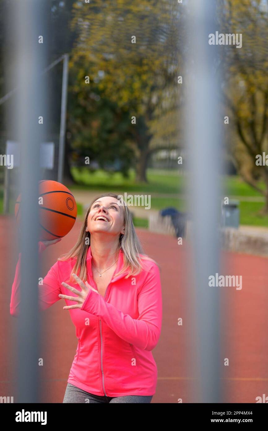 Bella donna bionda in procinto di saltare con il basket in mano su un campo sportivo con un grande sorriso Foto Stock
