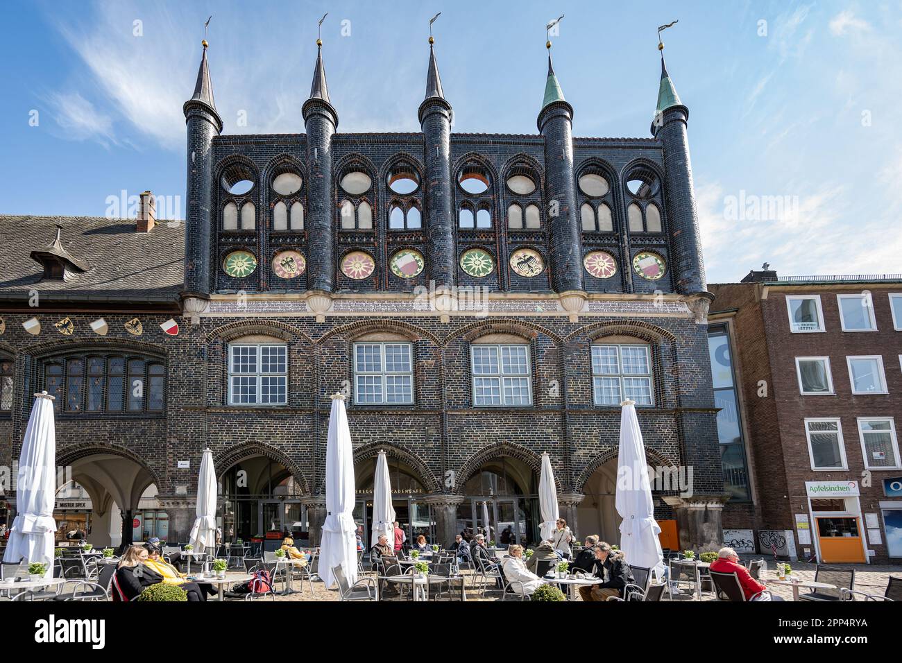Lubecca, Germania, 17 aprile 2023: Facciata dello storico municipio di Lubecca in mattoni scuri alla piazza del mercato con un caffè di strada nel vecchio Foto Stock