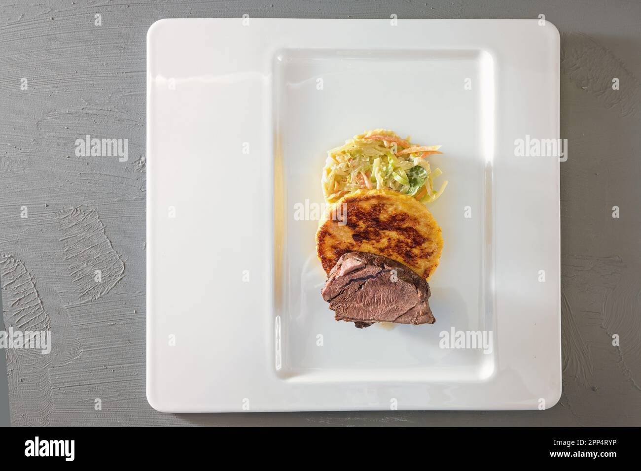 Arrosto di cervo, gnocchi di pane piatto e verdure a forma di cavolo rotondo, piatto gourmet su un piatto bianco, sfondo grigio, vista ad angolo alto dall'alto, cop Foto Stock