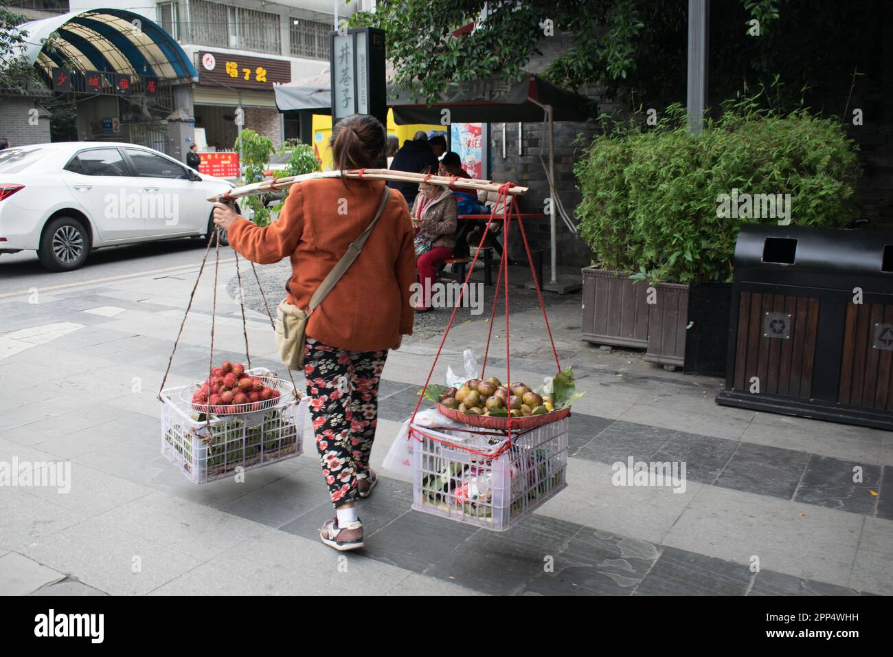 La schiena di una donna cinese porta fichi e rambutani in vendita su cestini appesi su un bastone sulle sue spalle - Chengdu, Cina. Foto Stock