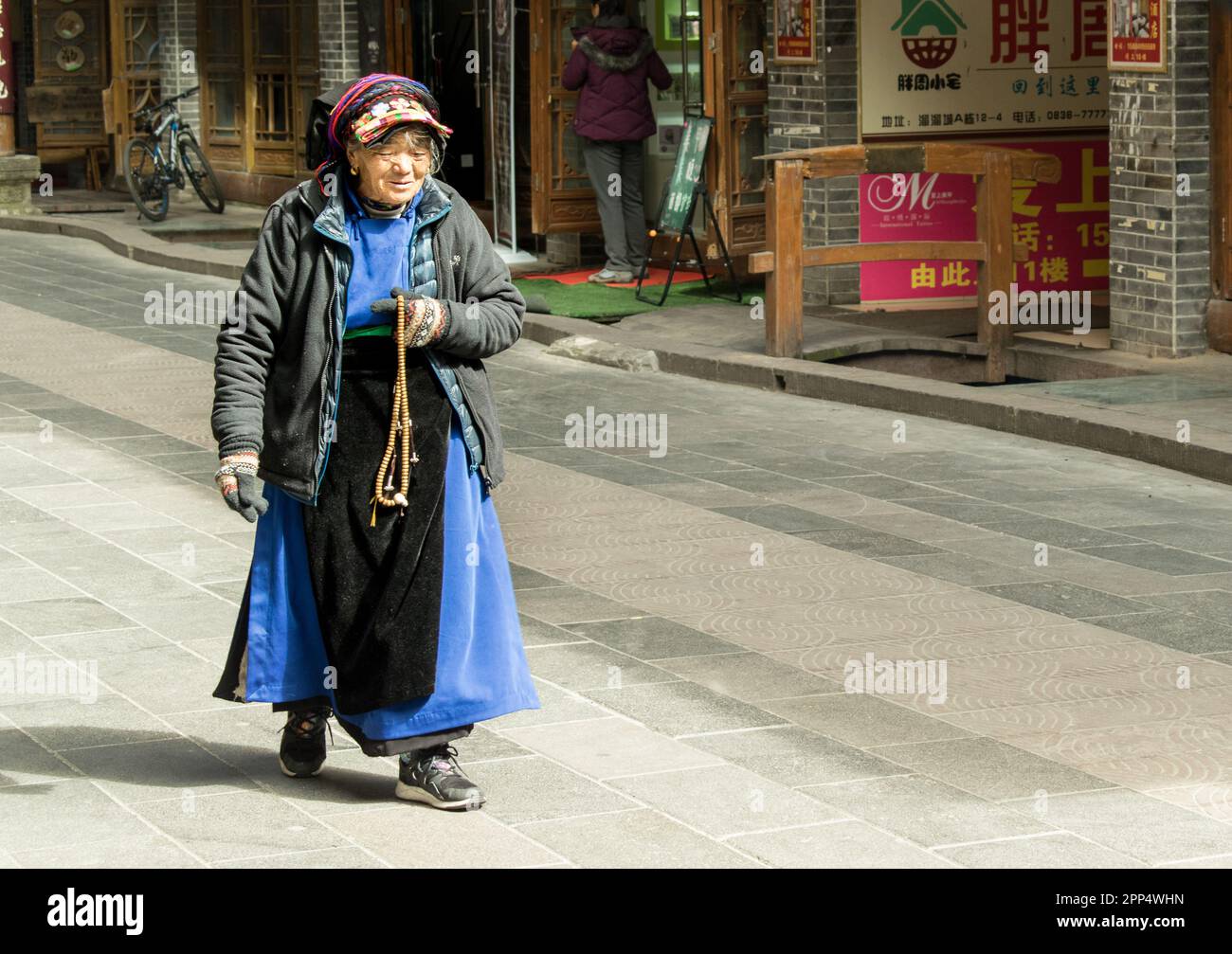 Donna anziana cammina per strada con perline di preghiera tibetane chiamate Mala. Foto Stock