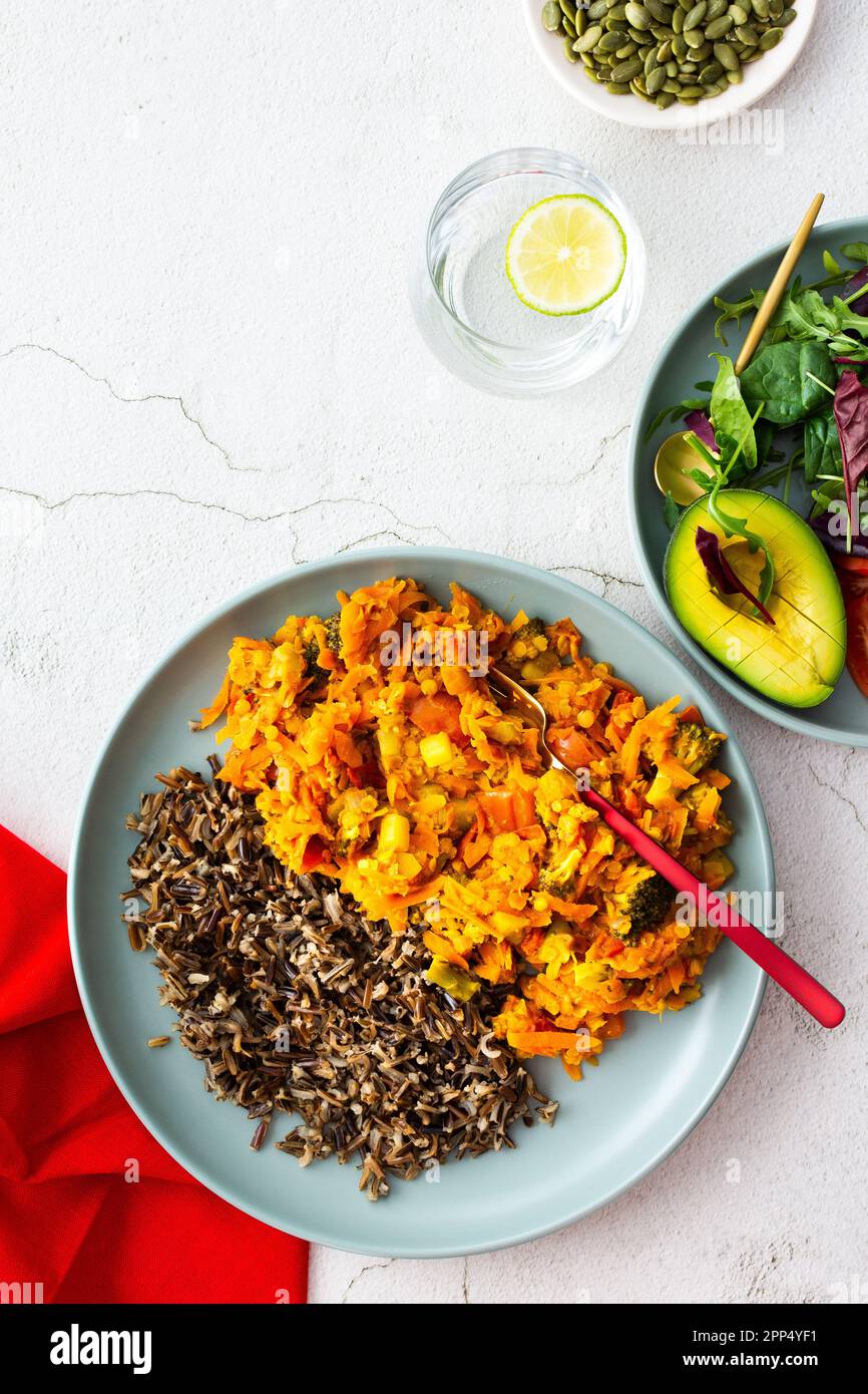 Pranzi salutari, riso selvatico con carota e sugo di pomodoro, broccoli e cipolla, insalata fresca mista con semi di zucca, acqua al limone, vista dall'alto Foto Stock