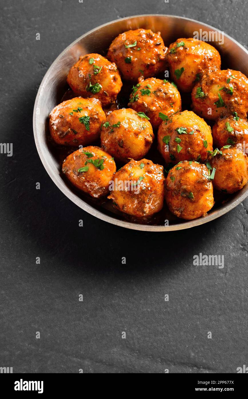 Patate Bombay. Padella le patate fritte con semi di jeera e coriandolo in una ciotola su fondo di pietra nera con spazio di testo libero. Popolare india Foto Stock
