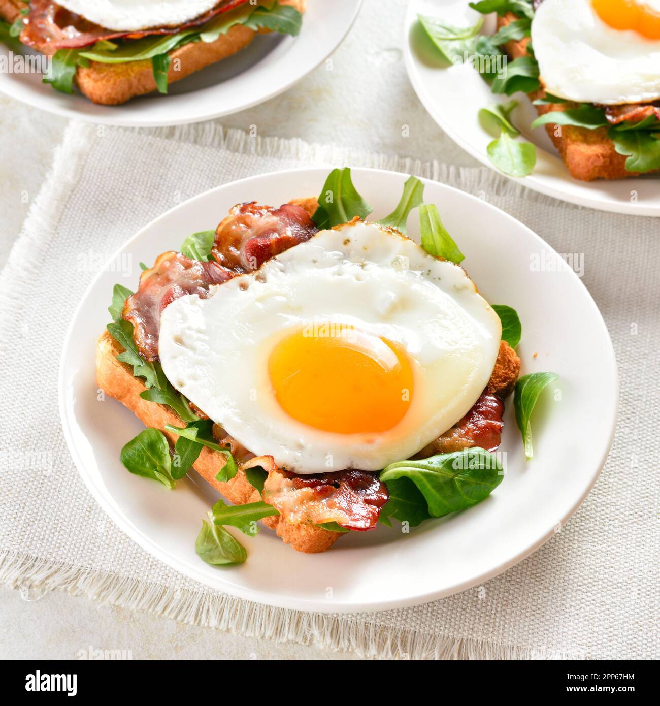 Apri i sandwich con uova fritte, pancetta e foglie di verdure sul piatto su sfondo di pietra chiaro. Vista ravvicinata Foto Stock