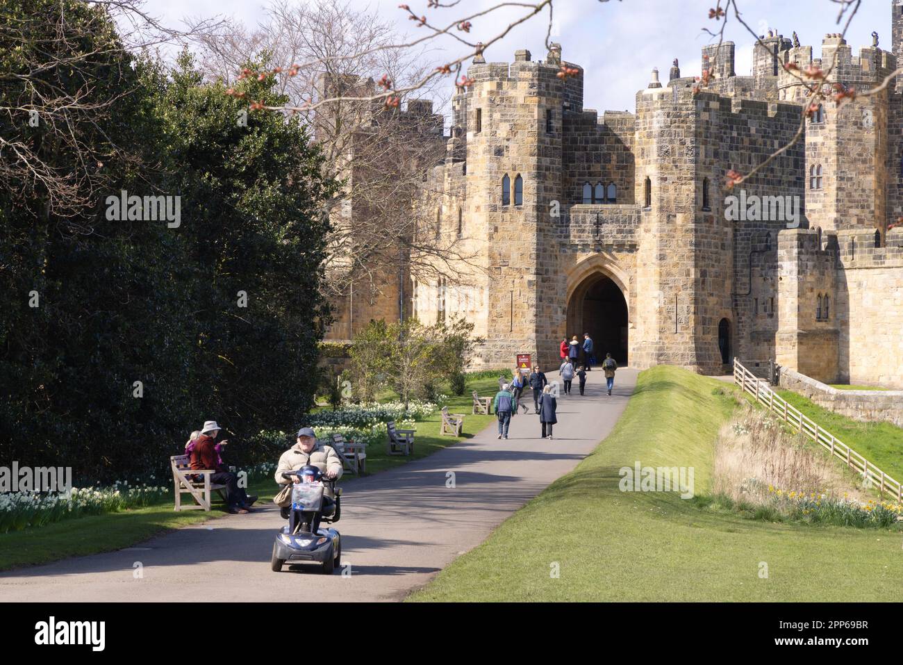 Ingresso al castello di Alnwick; con accesso per scooter per disabili; visitatori nei giardini del castello in una soleggiata giornata primaverile; Alnwick Northumberland Inghilterra Regno Unito Foto Stock