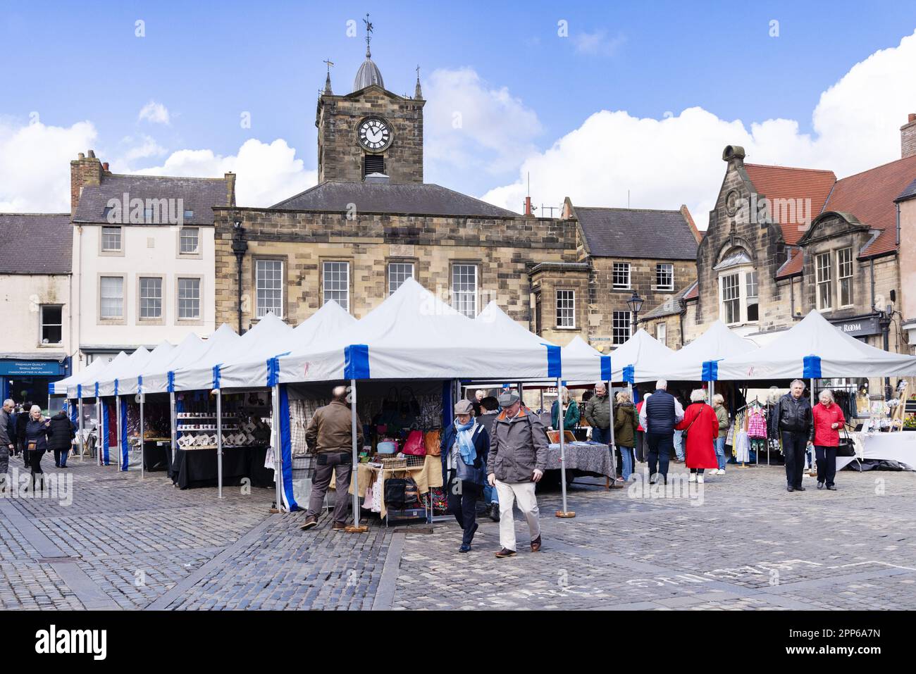 Mercato di Alnwick; gente che acquista alle bancarelle del mercato nella Piazza del mercato, sotto il sole della primavera; centro di Alnwick, Alnwick, Northumberland Regno Unito Foto Stock