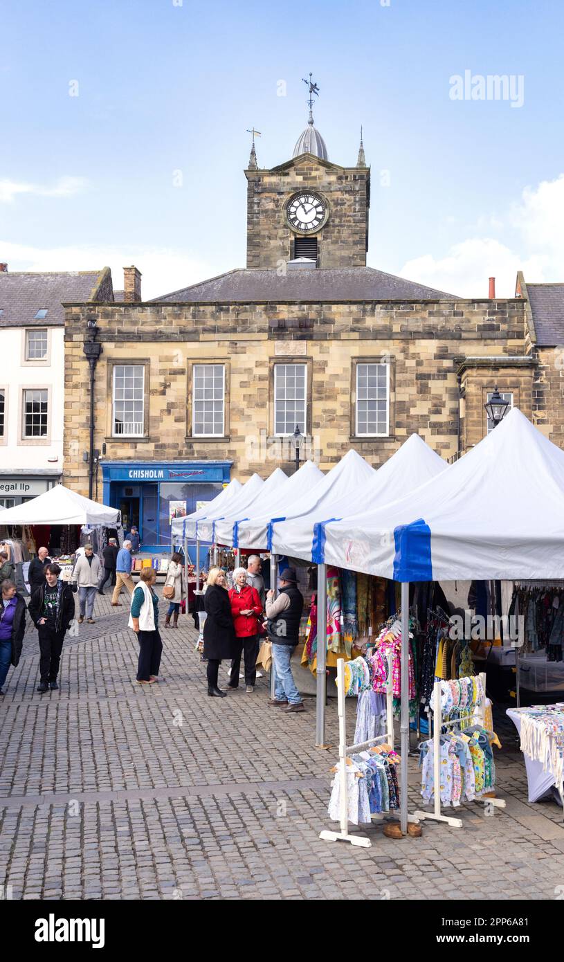 Mercato di Alnwick; gente che acquista alle bancarelle del mercato nella Piazza del mercato, sotto il sole della primavera; centro di Alnwick, Alnwick, Northumberland Regno Unito Foto Stock