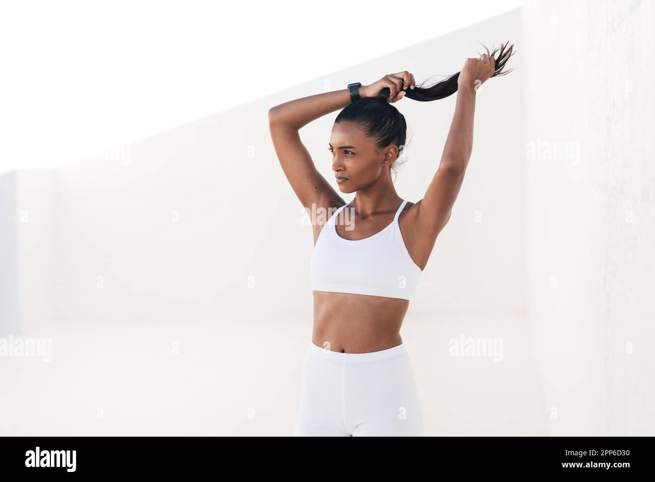 Atleta snella donna che regola il suo ponytail mentre è in piedi in studio all'aperto Foto Stock