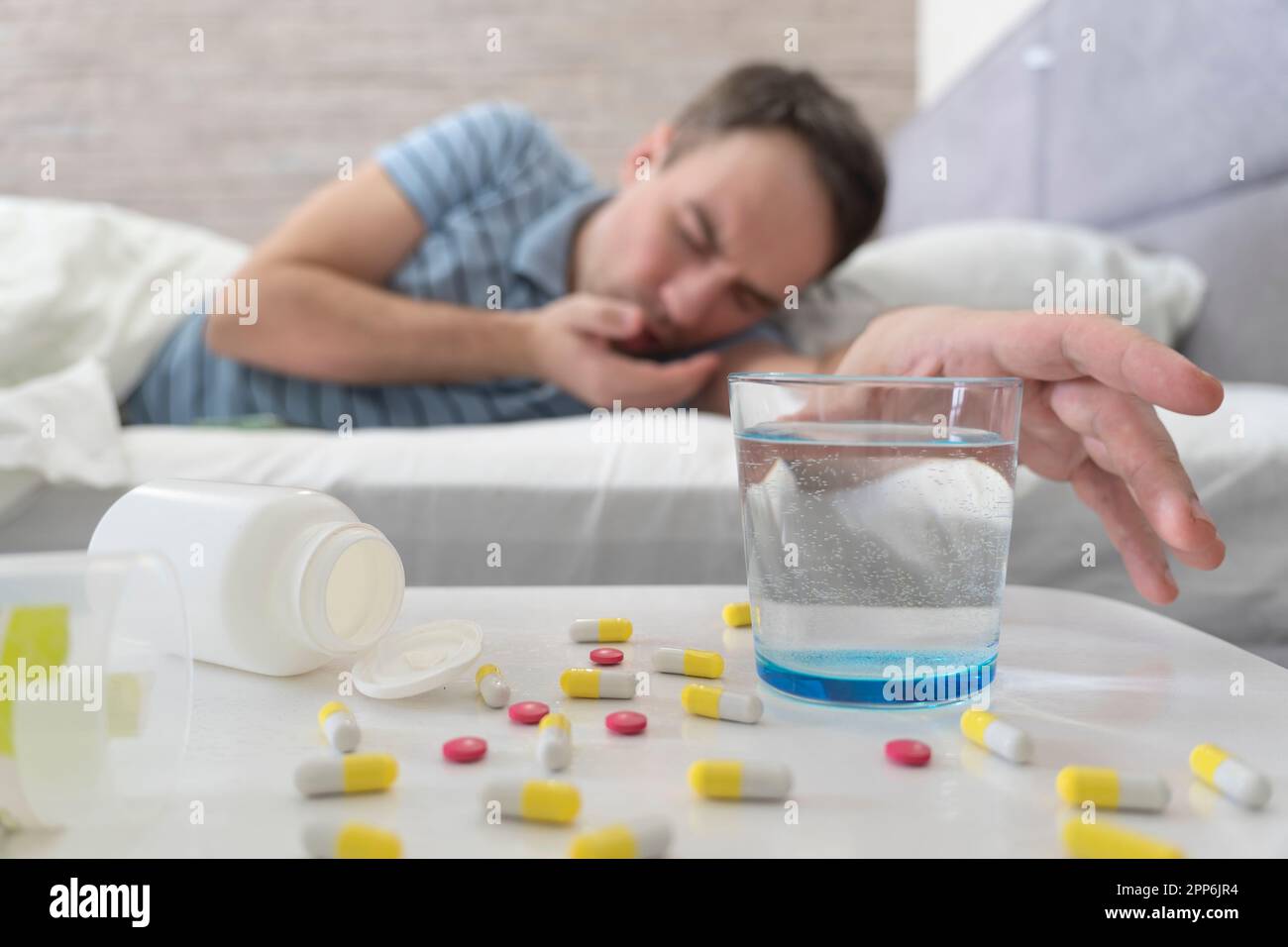 Sbornia. L'uomo prende la pillola e l'acqua. Uomo a letto mal di testa mattutino. Uomo che usa Aspirin. Bicchiere d'acqua Close Up. il sintomo è avvelenamento da cibo. Foto Stock