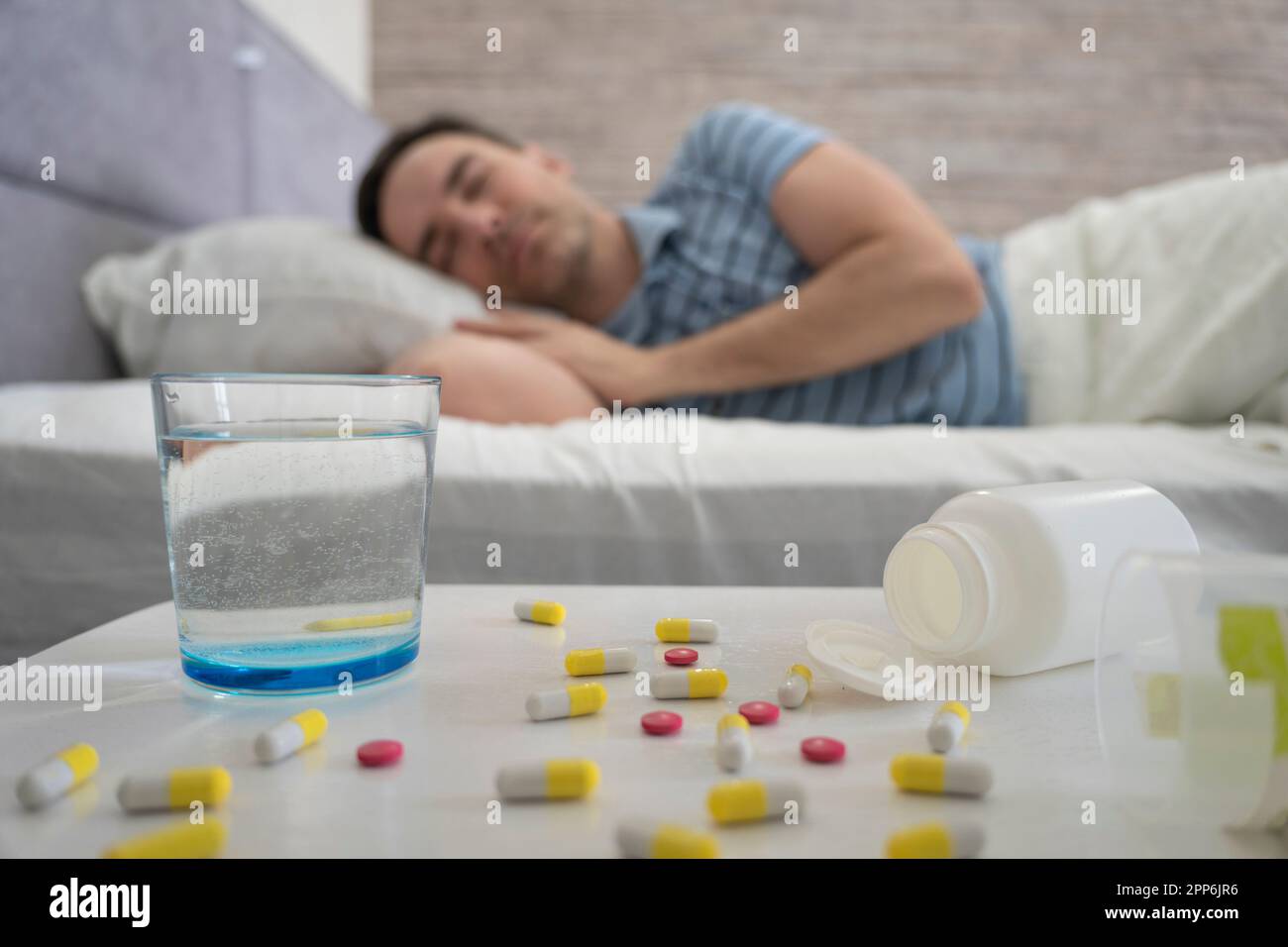 Uomo che dorme - pillole sul tavolo da letto. un uomo dorme su un letto durante il giorno in primo piano è un tavolo con pillole e un bicchiere d'acqua. Sonniferi f Foto Stock