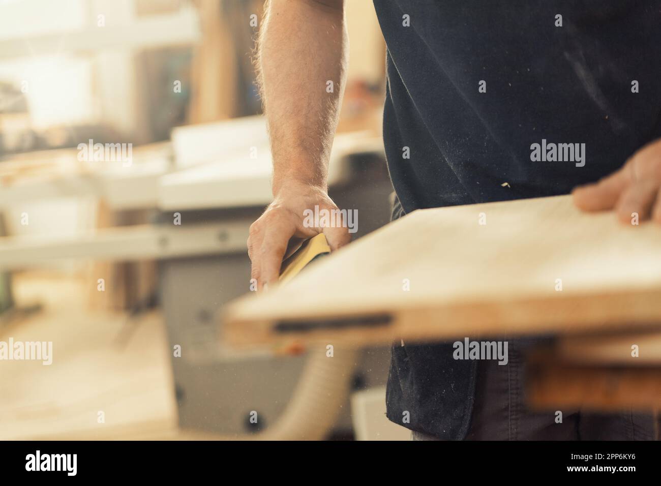 Il braccio dell'artigiano del legno che tiene un metro a nastro è a fuoco mentre si prepara a lavorare sul legno davanti a lui, pronto a costruire mobili. Il suo braccio è s. Foto Stock