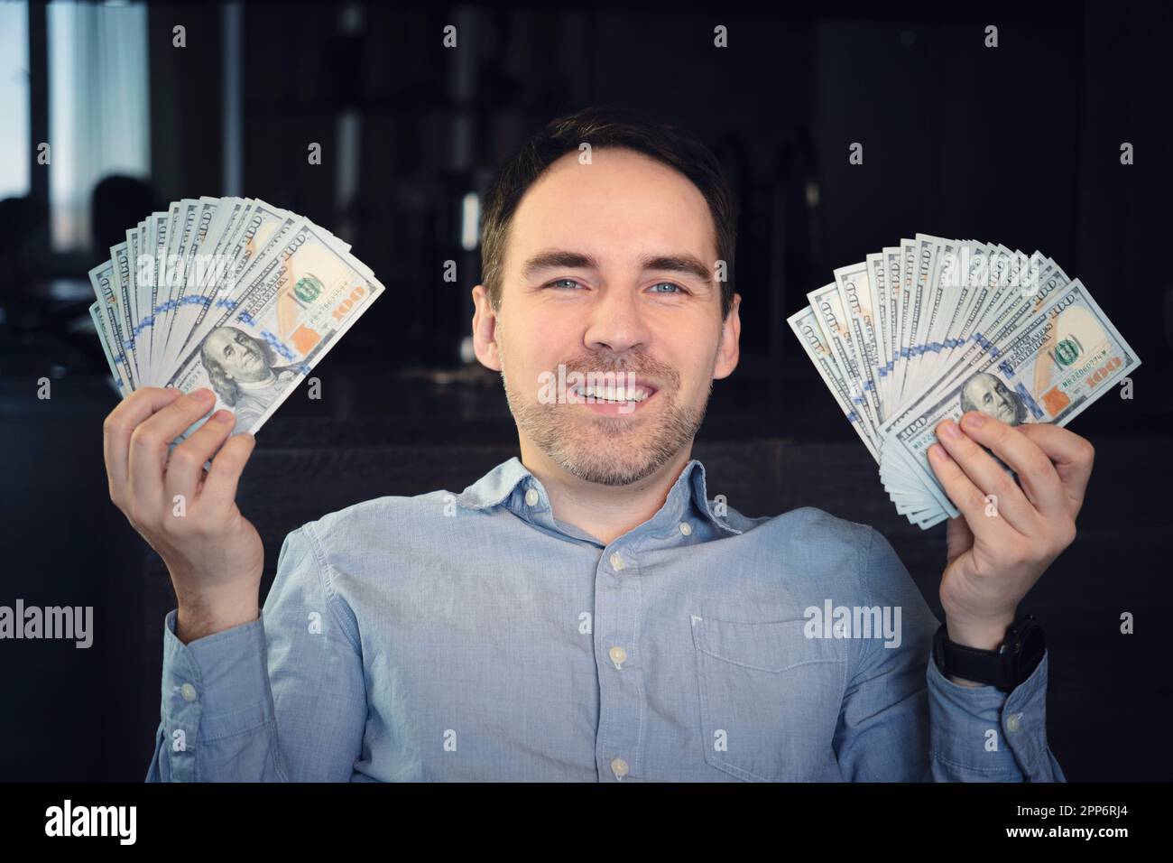 Mani che tengono contanti del dollaro. 1000 dollari in 100 fatture in primo piano di una mano dell'uomo su uno sfondo scuro. Foto Stock