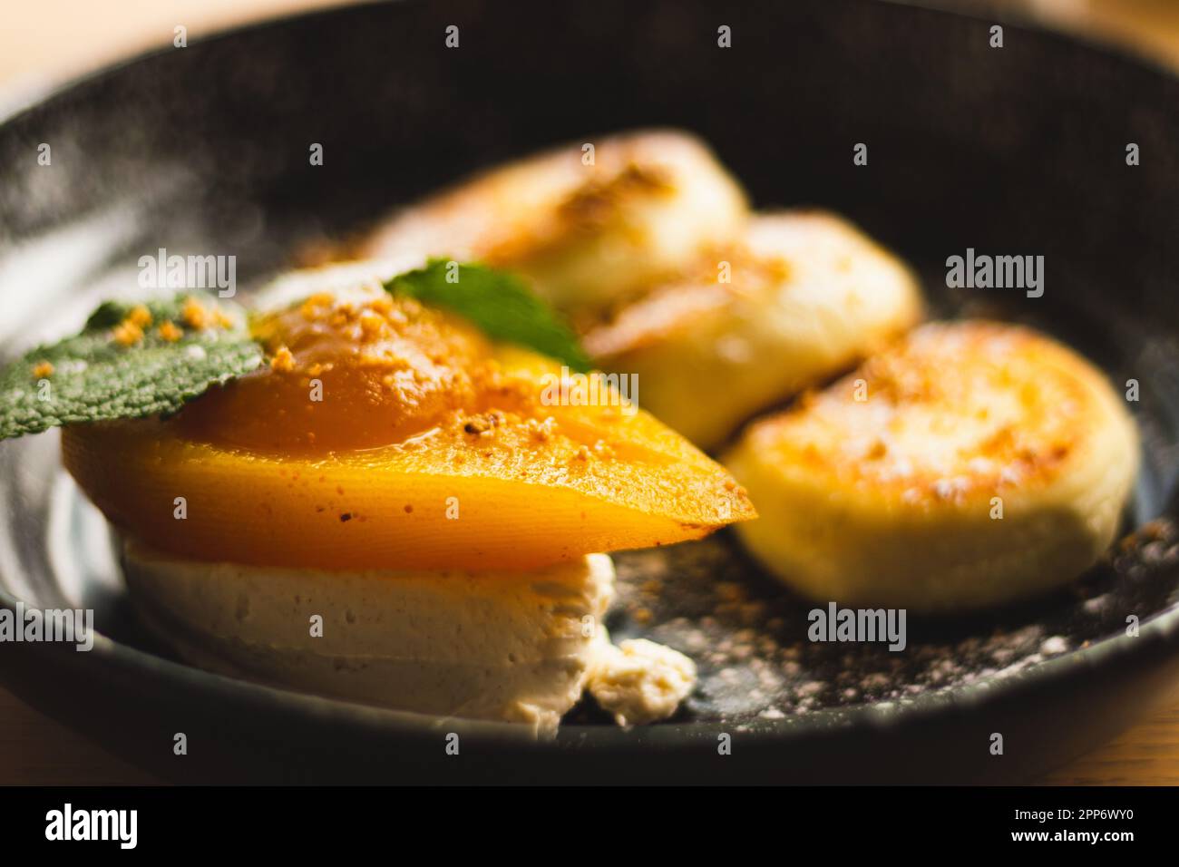 Syrniki con pera al caramello e ricotta. Frittelle cagliate su piatto nero. Colazione deliziosa. Cibo ucraino. Pera al forno con foglia di menta e frittella Foto Stock