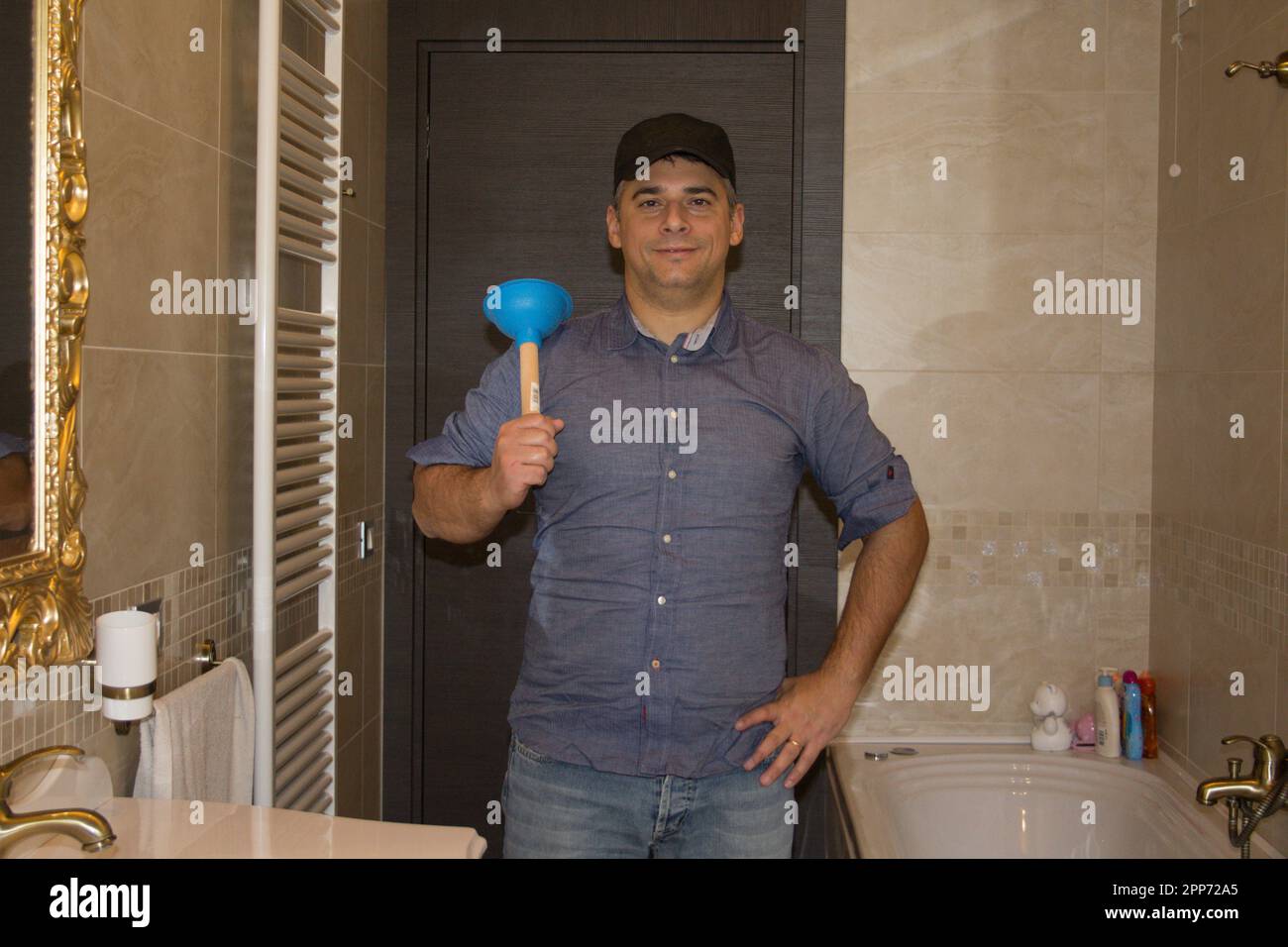 Immagine di un idraulico sorridente nel bagno di casa che tiene uno stantuffo in mano mentre si stanca un lavandino. Fai da te a casa. Foto Stock