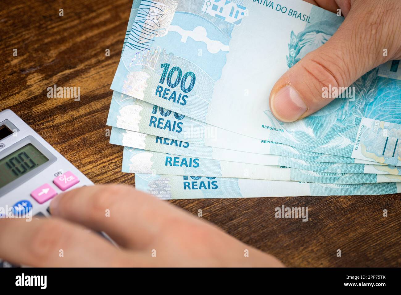 L'uomo tiene i soldi brasiliani, rais e conta sulle spese o calcolatore di guadagni, concetto finanziario, bilanci domestici in Brasile Foto Stock
