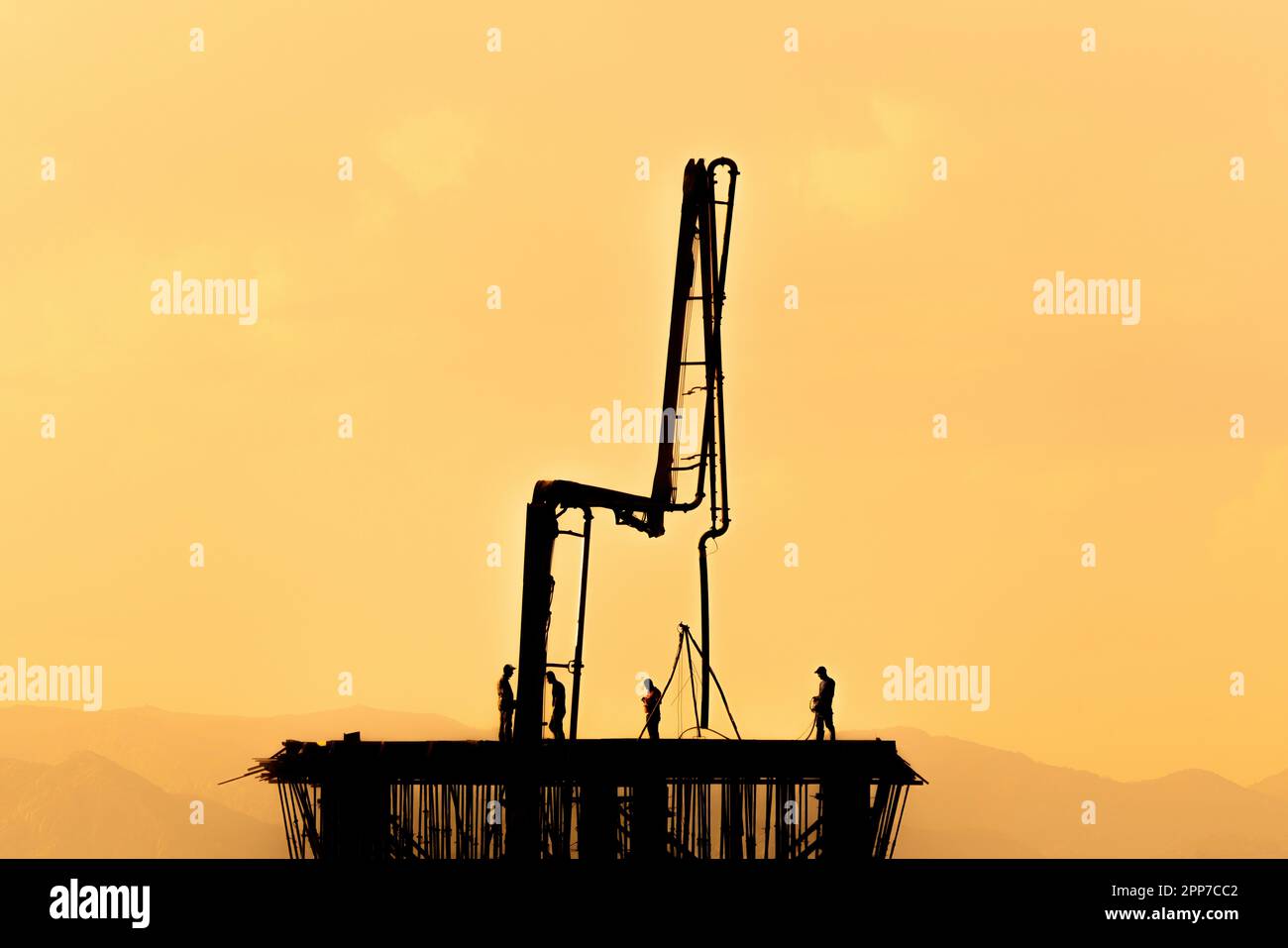 Lavoratori che versano calcestruzzo ad un cantiere di costruzione. Luce di retromarcia, silhouette Foto Stock