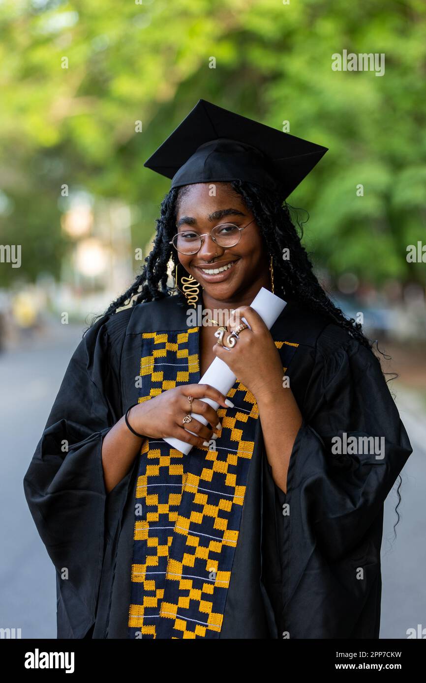 Ritratto di Black Female African University Graduate con abito nero e berretto, in possesso del suo diploma di laurea, fiero di risultati accademici e su Foto Stock