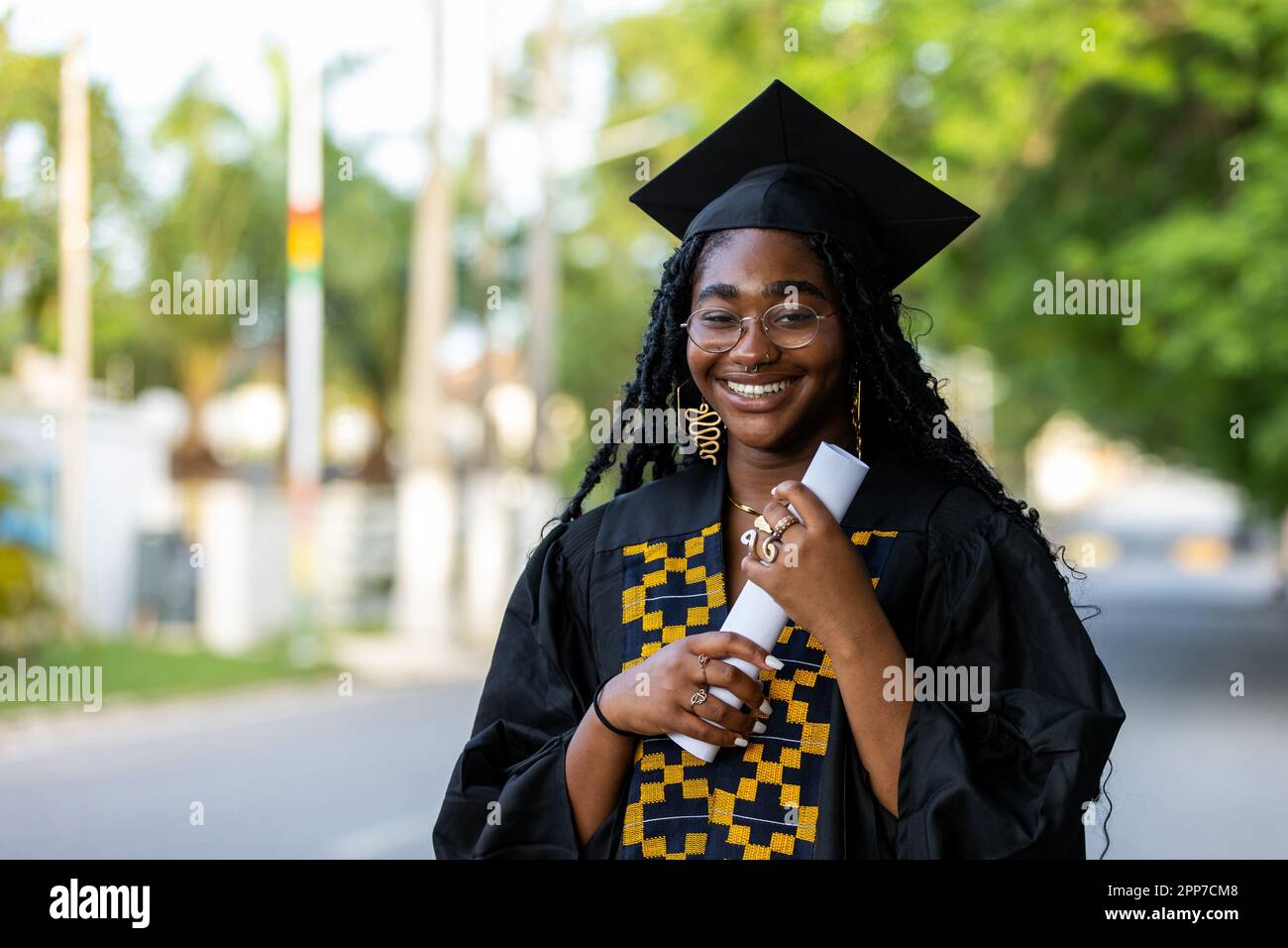 Ritratto di Black Female University Graduate vestito e berretto nero, con il suo diploma di laurea, orgoglioso del successo accademico e af Foto Stock