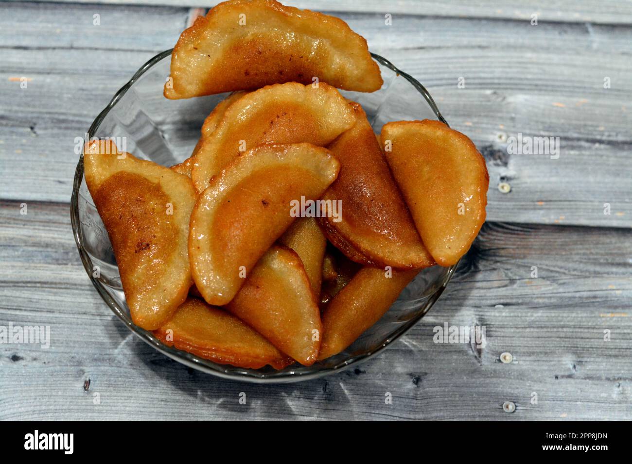 Una ciotola di gnocchi di qatayef farciti e riempiti di noci e di cocco grattugiato fritto in olio profondo e imbevuto di sciroppo di zucchero, panna piegata per dessert arabo Foto Stock