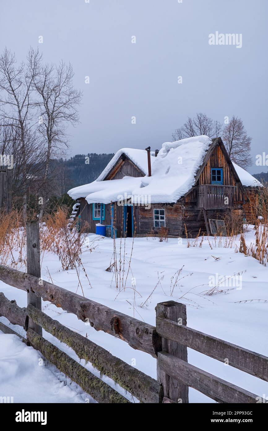 Vecchia casa in legno abbandonata. Il tetto è ricoperto da uno spesso strato di neve. Altai villaggio Ust'-Lebed' nella stagione invernale. Siberia, Russia. Foto Stock