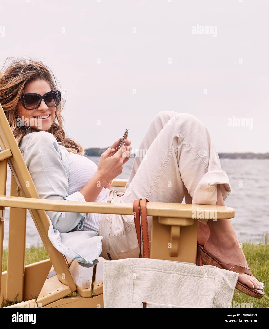 In movimento lento e sicuro si sente bene. una giovane donna attraente che usa uno smartphone mentre si rilassa vicino al lago. Foto Stock