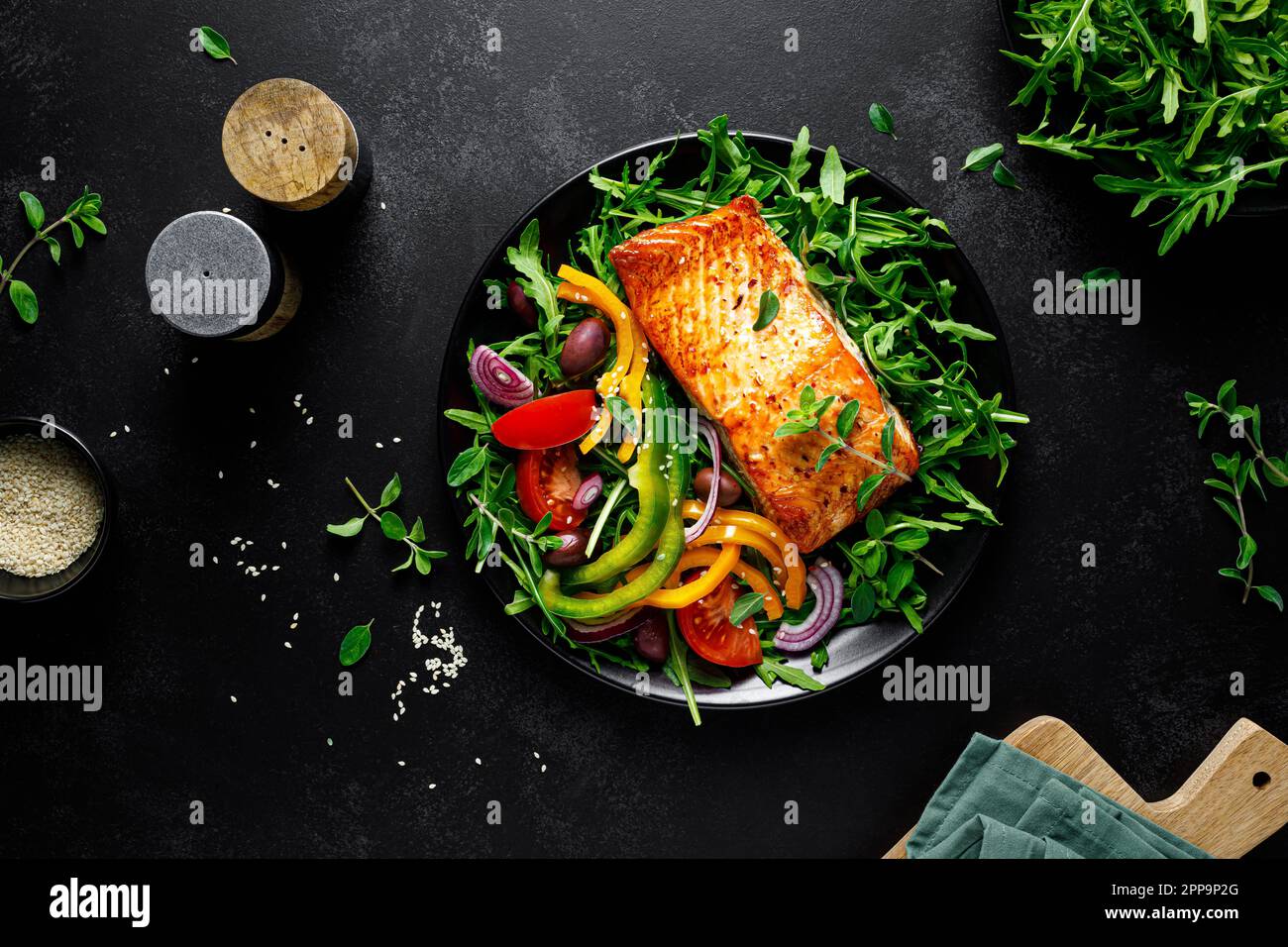 Filetto di salmone alla griglia e insalata verde di verdure fresche di rucola con pomodori, olive e peperone su sfondo nero, cibo sano, mediterranea Foto Stock